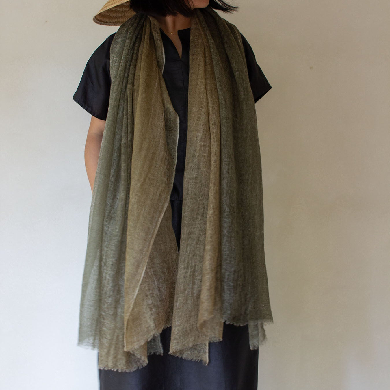 A person wearing a dip-dyed green cashmere scarf with a gradient of green and yellow tones, paired with a black top and a hat.