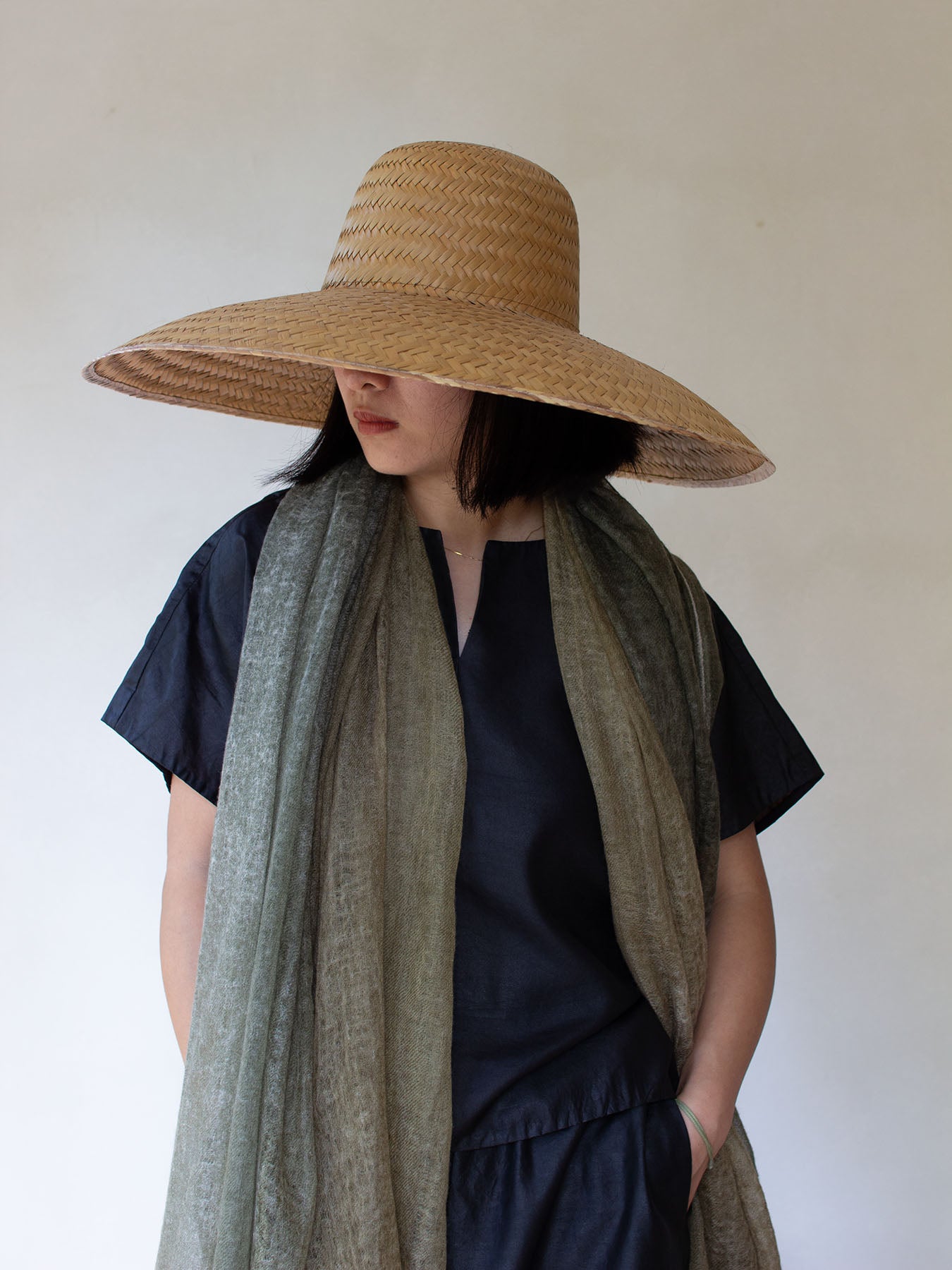 A person wearing a dip-dyed green cashmere scarf with a gradient of green and yellow tones, paired with a black top and a hat.