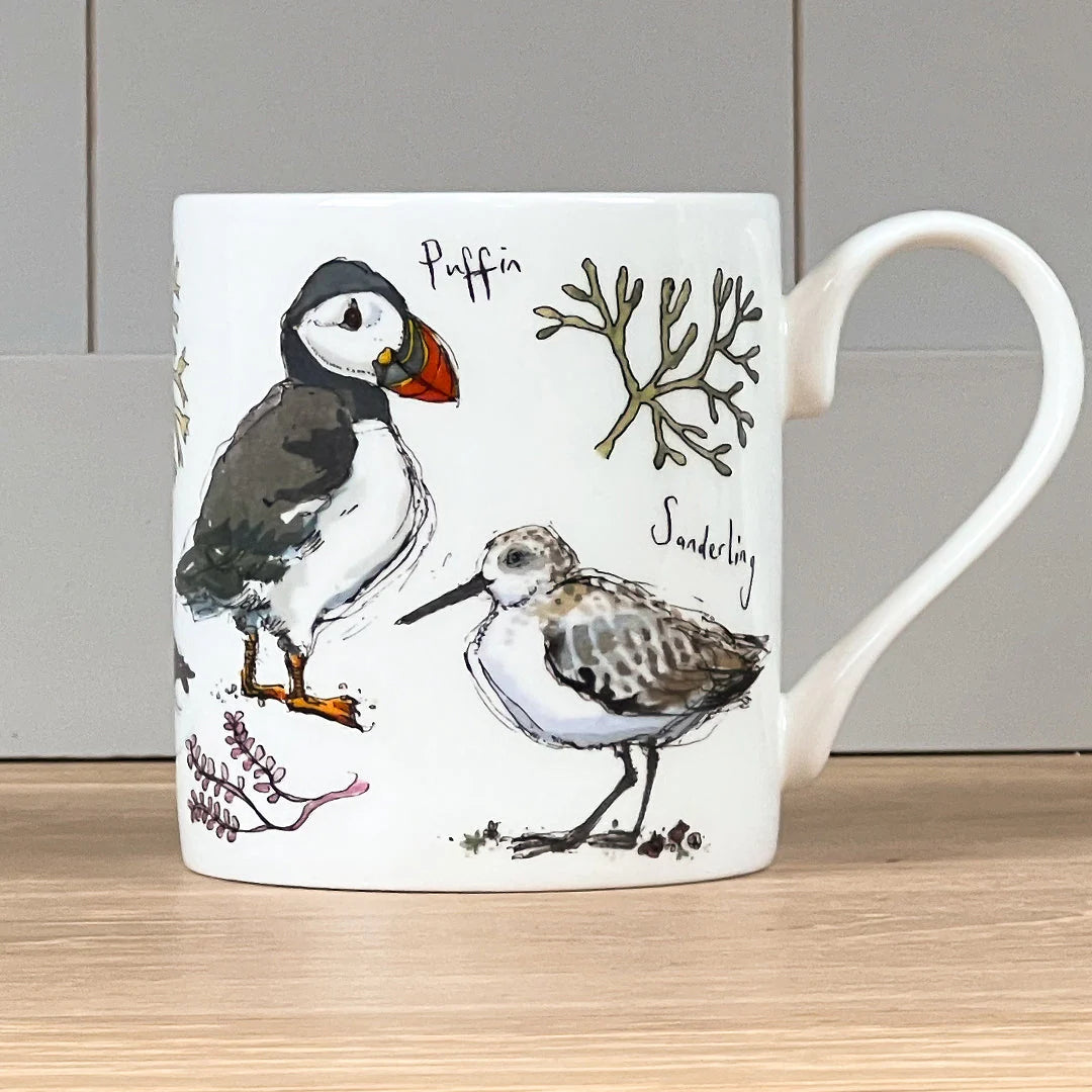 Mug with illustrations of a puffin and sandpiper on a wooden surface.