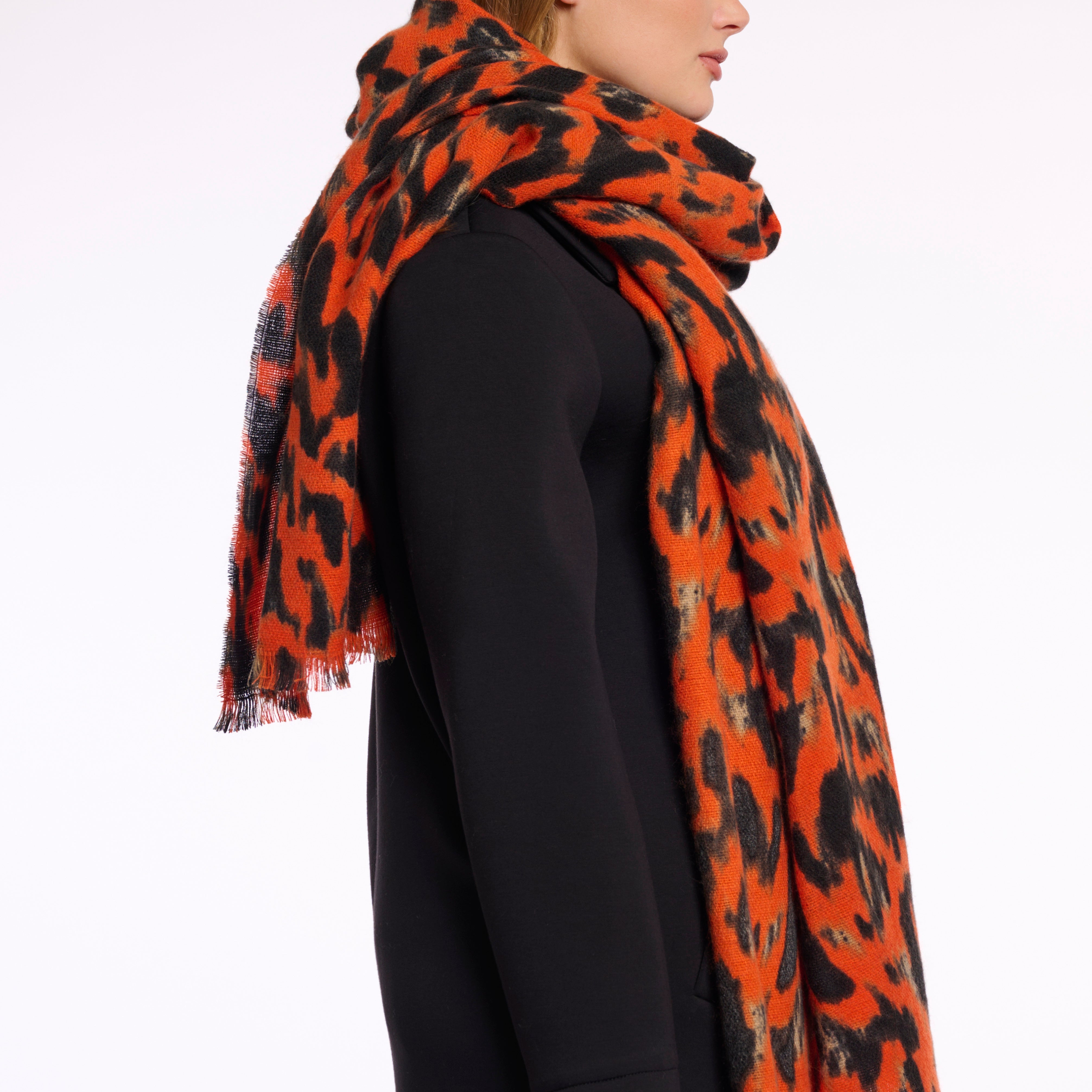 Person wearing a large orange and black patterned scarf on a white background