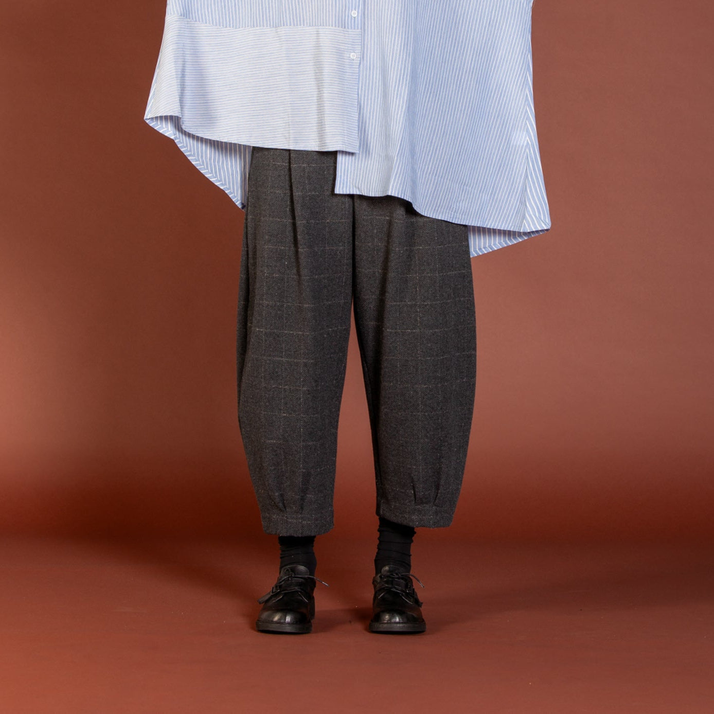 Woman wearing a light blue oversized shirt and gray plaid pants against a brown background