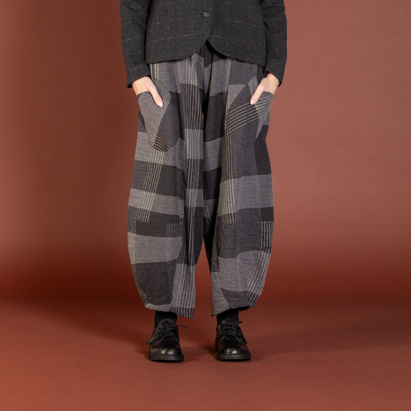 Person wearing plaid pants and a dark jacket on a brown background