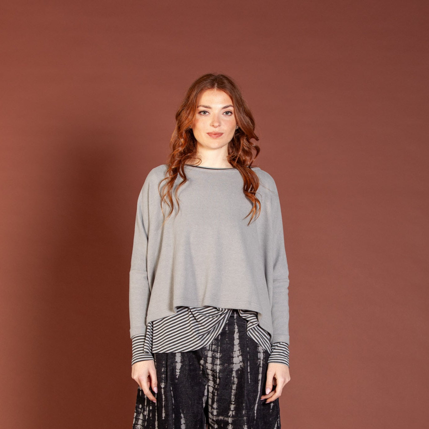 Woman wearing a gray sweater and black tie-dye pants against a brown background