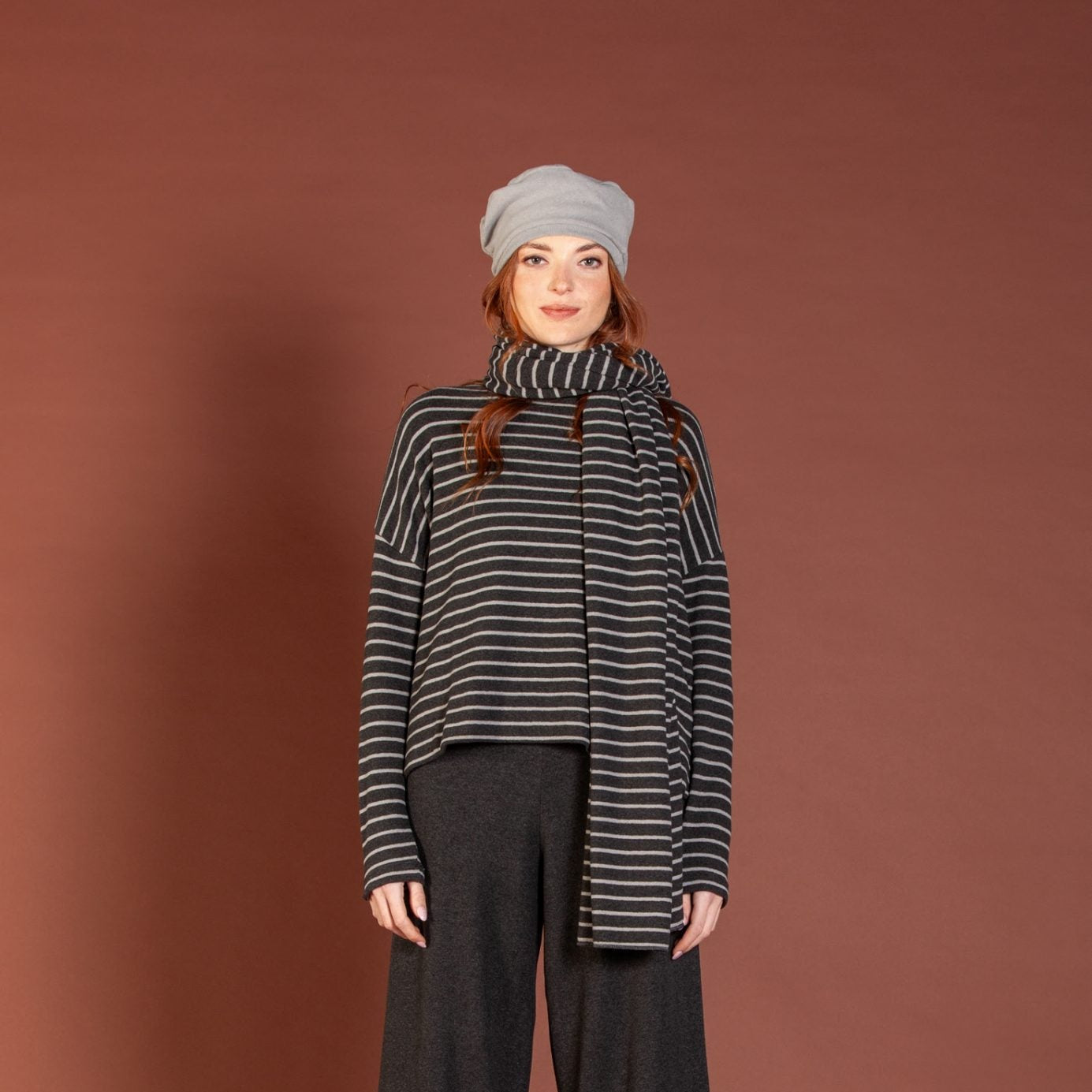 Person wearing a striped sweater, gray pants, and a gray beanie against a brown background