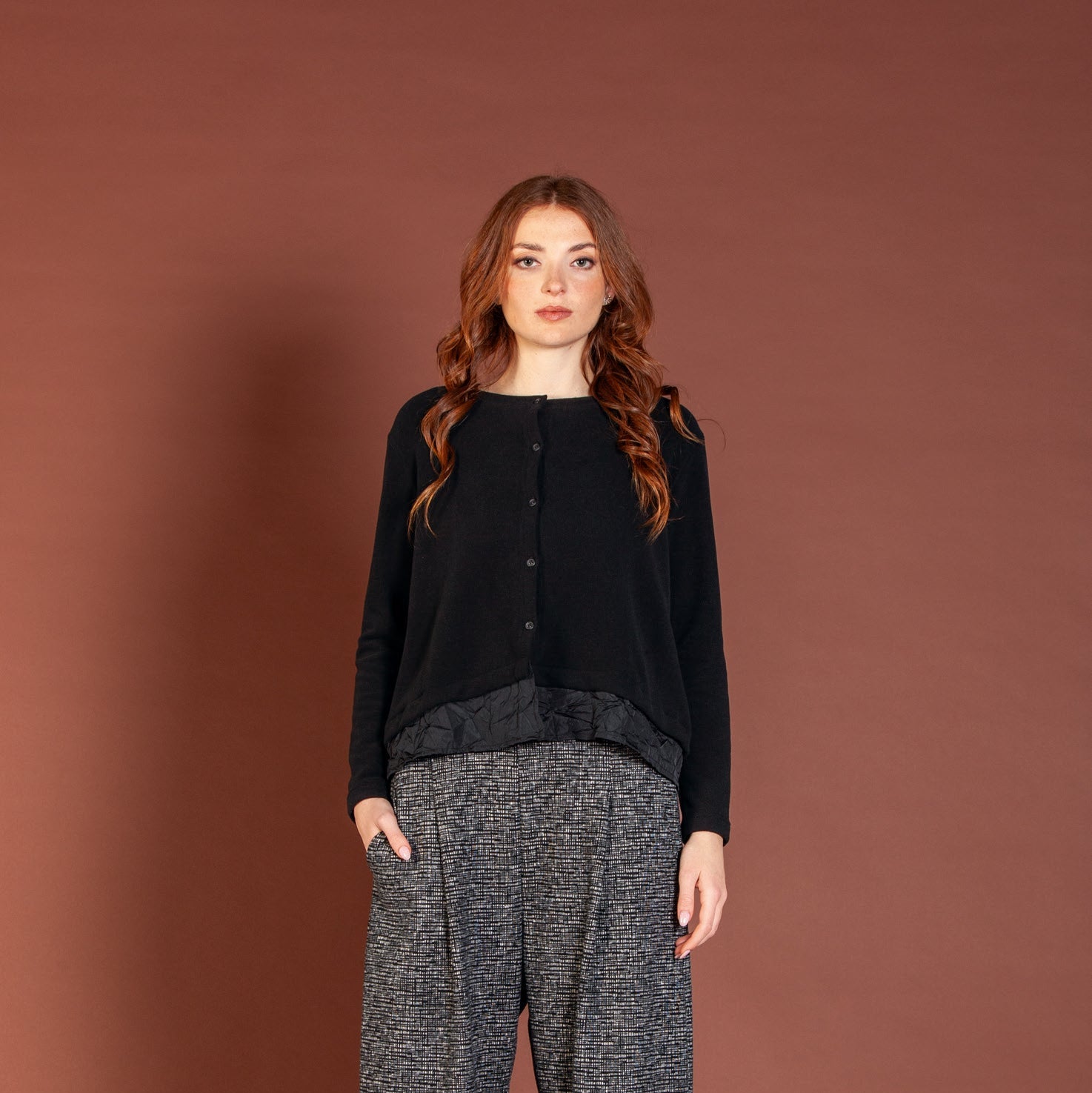 Woman wearing a black top and gray patterned pants against a brown background