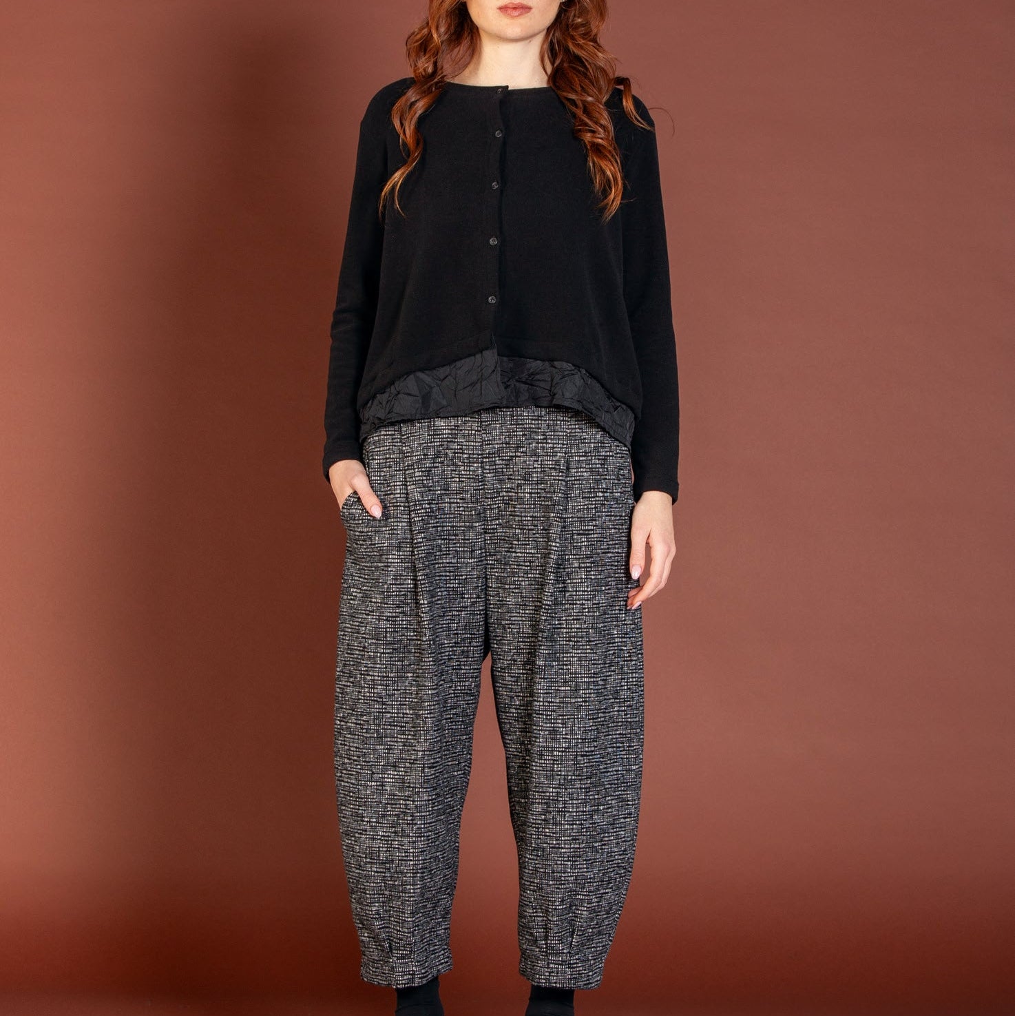Woman wearing a black top and gray patterned pants against a brown background