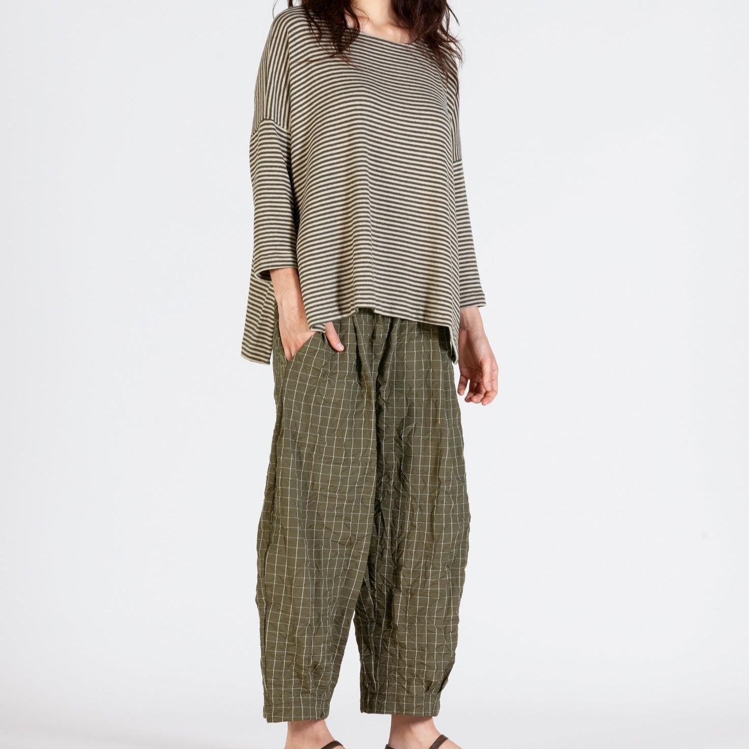Olive green gingham pants and a beige and brown horizontally striped loose-fitting top.
