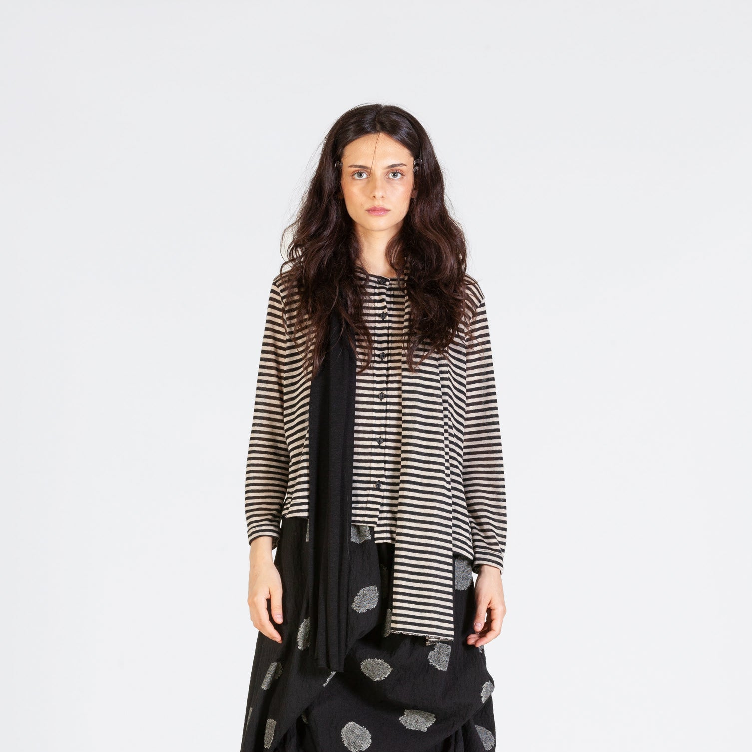 Woman modeling a beige and black striped shirt layered over a black polka dot asymmetrical skirt and black scarf.