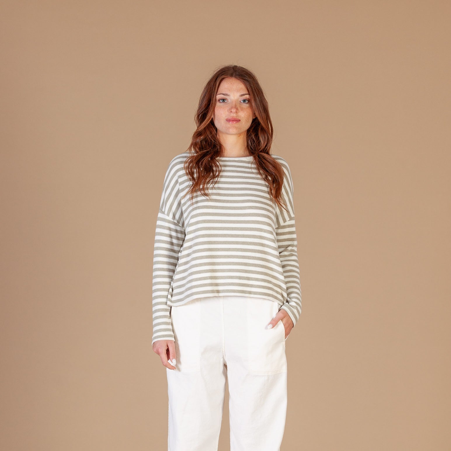 Woman wearing a striped sweater and white pants against a beige background