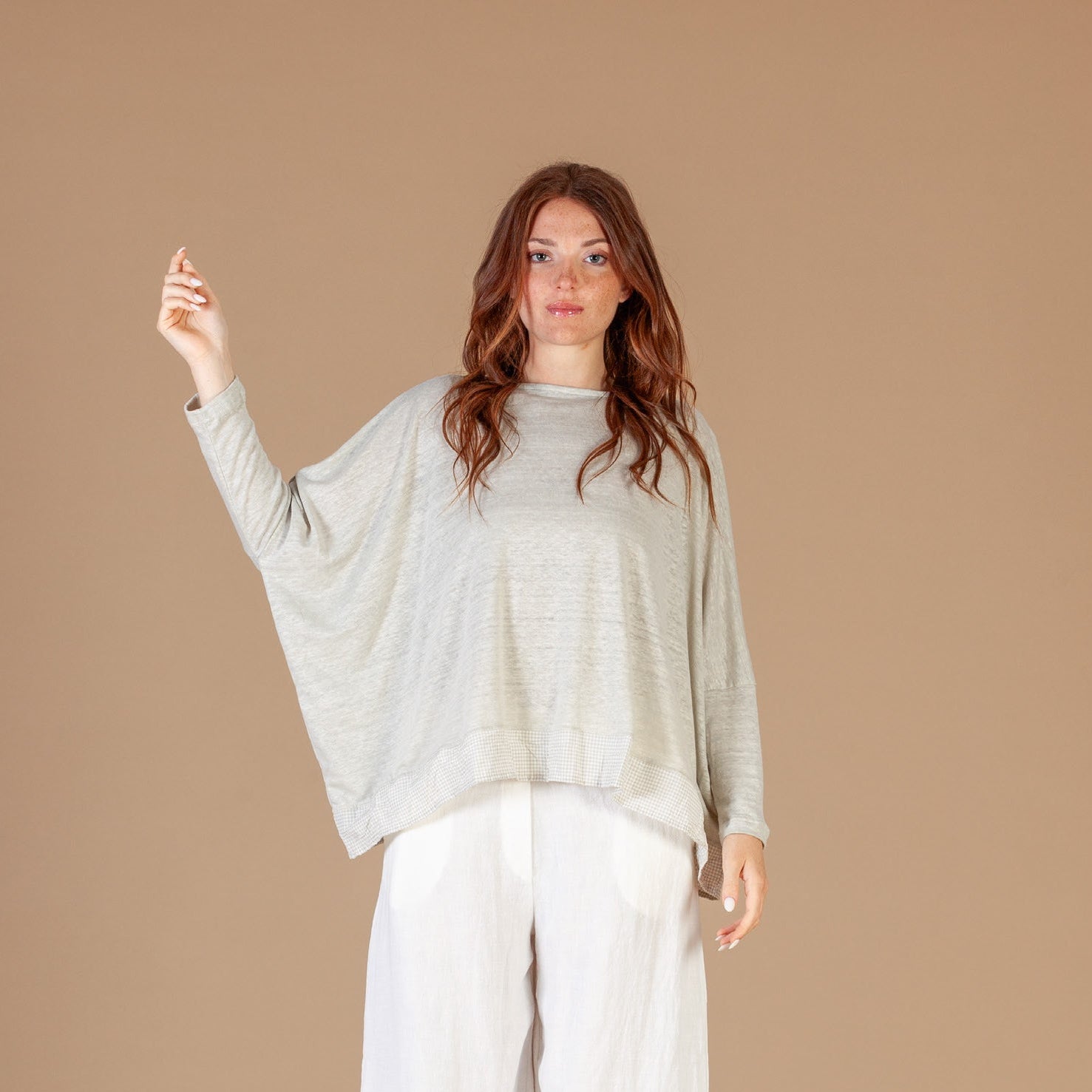 Woman wearing a light gray sweater and white pants against a beige background