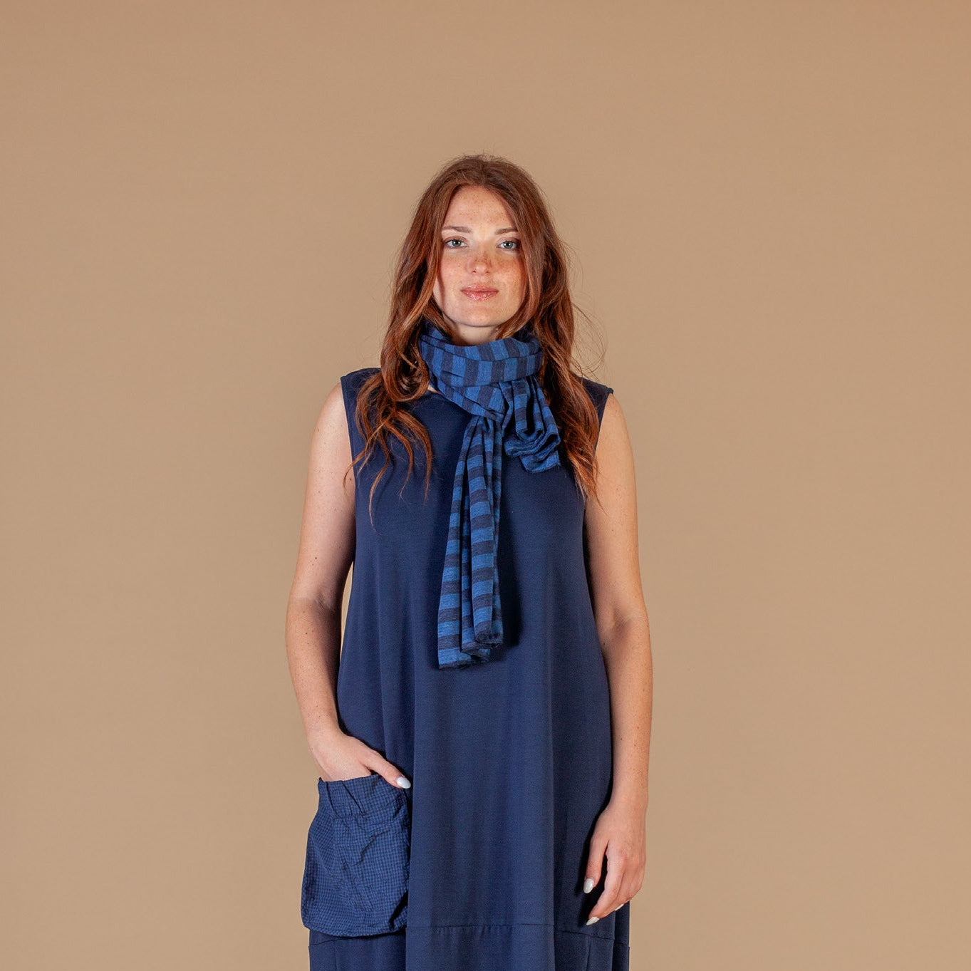 Woman wearing a blue dress with a matching scarf against a beige background