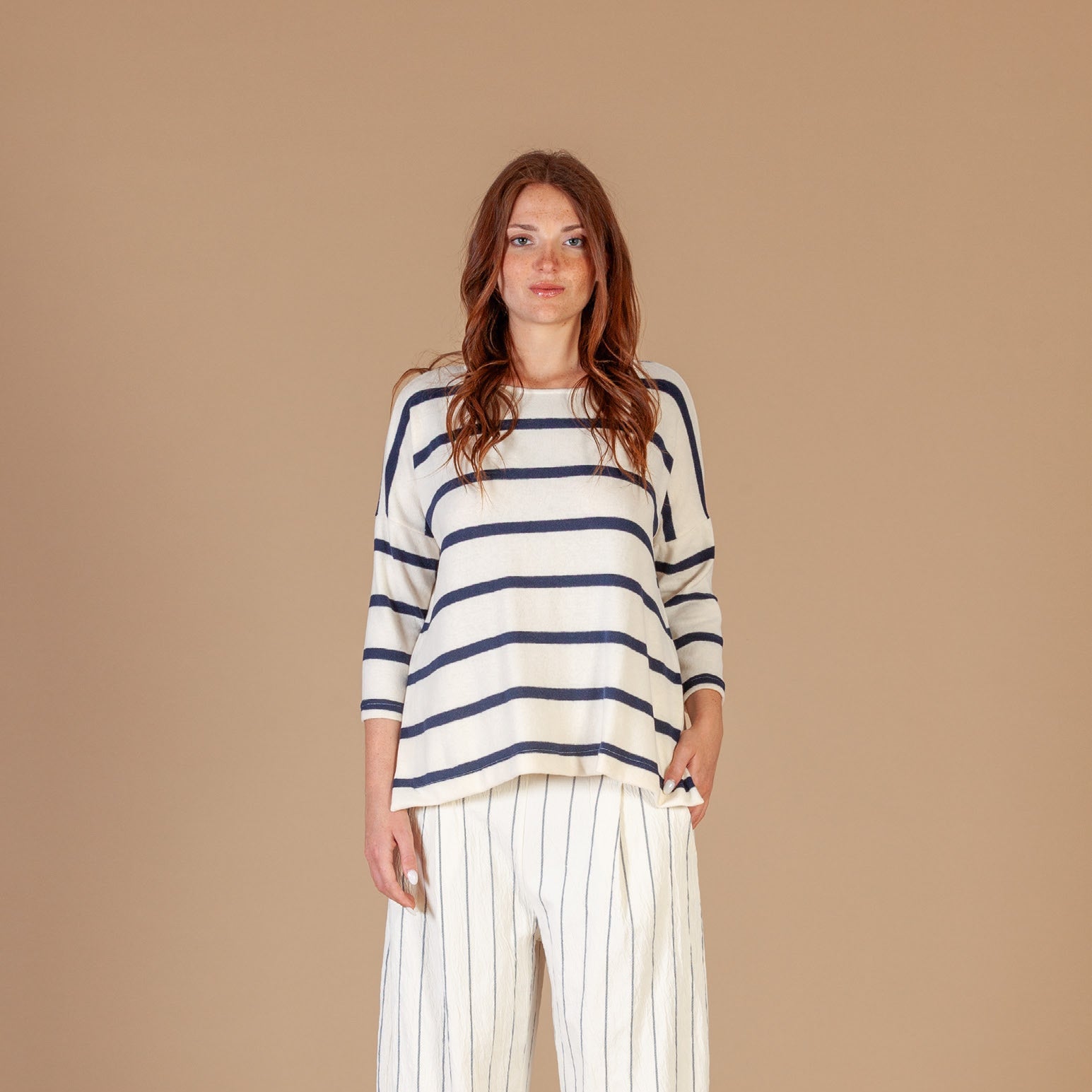 Women wearing a cream and blue striped relaxed fit jumper with white pinstripe trousers. 