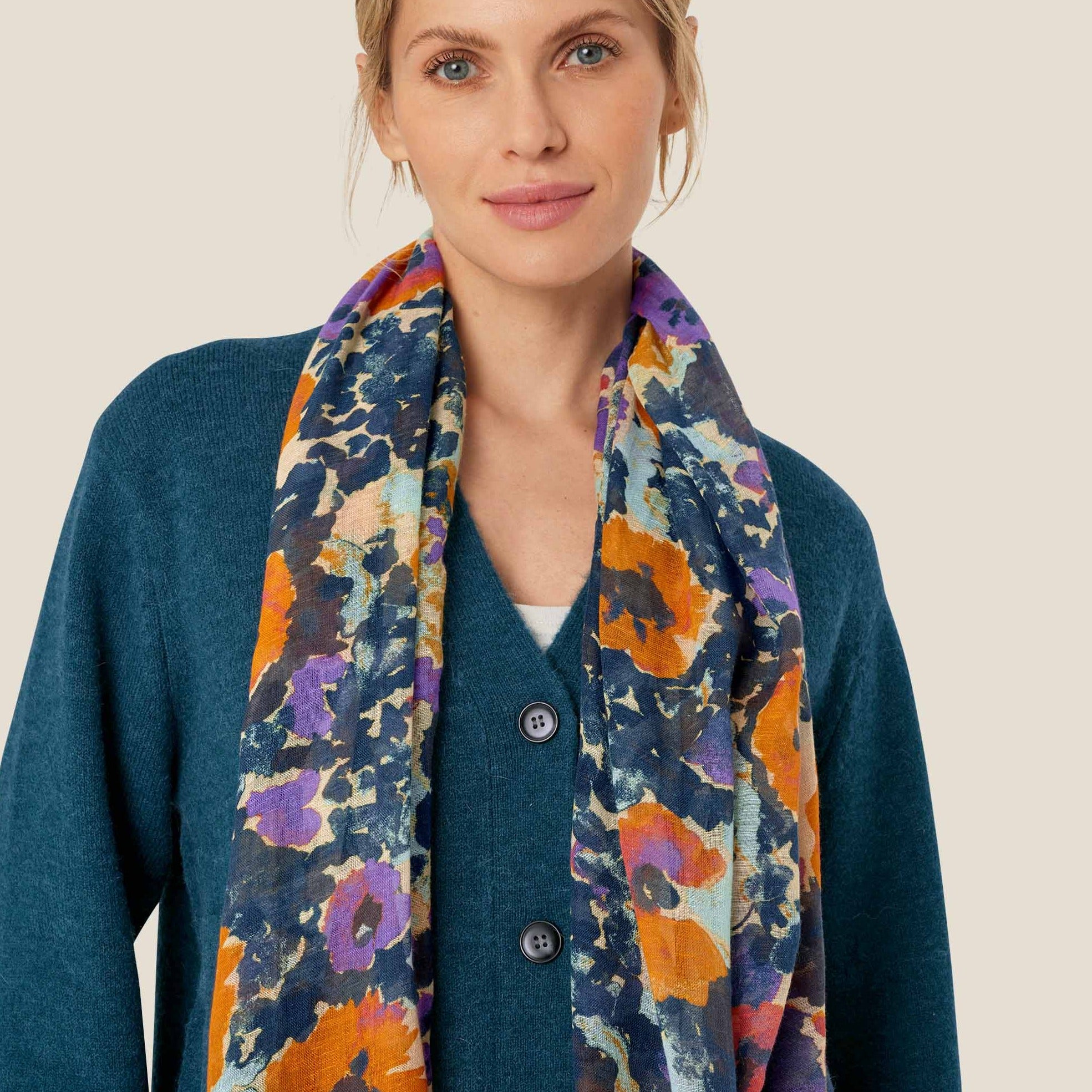Floral print scarf in teal, orange, purple, and cream.  The scarf is draped around a teal cardigan.
