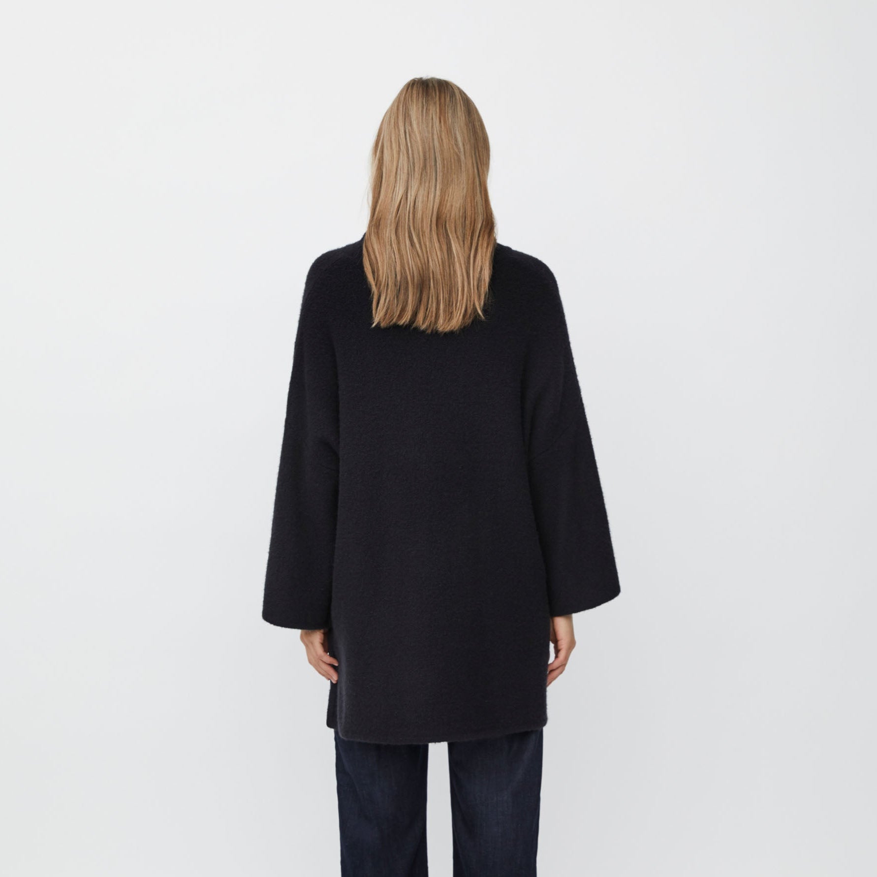 Person wearing a black tunic and dark jeans on a white background