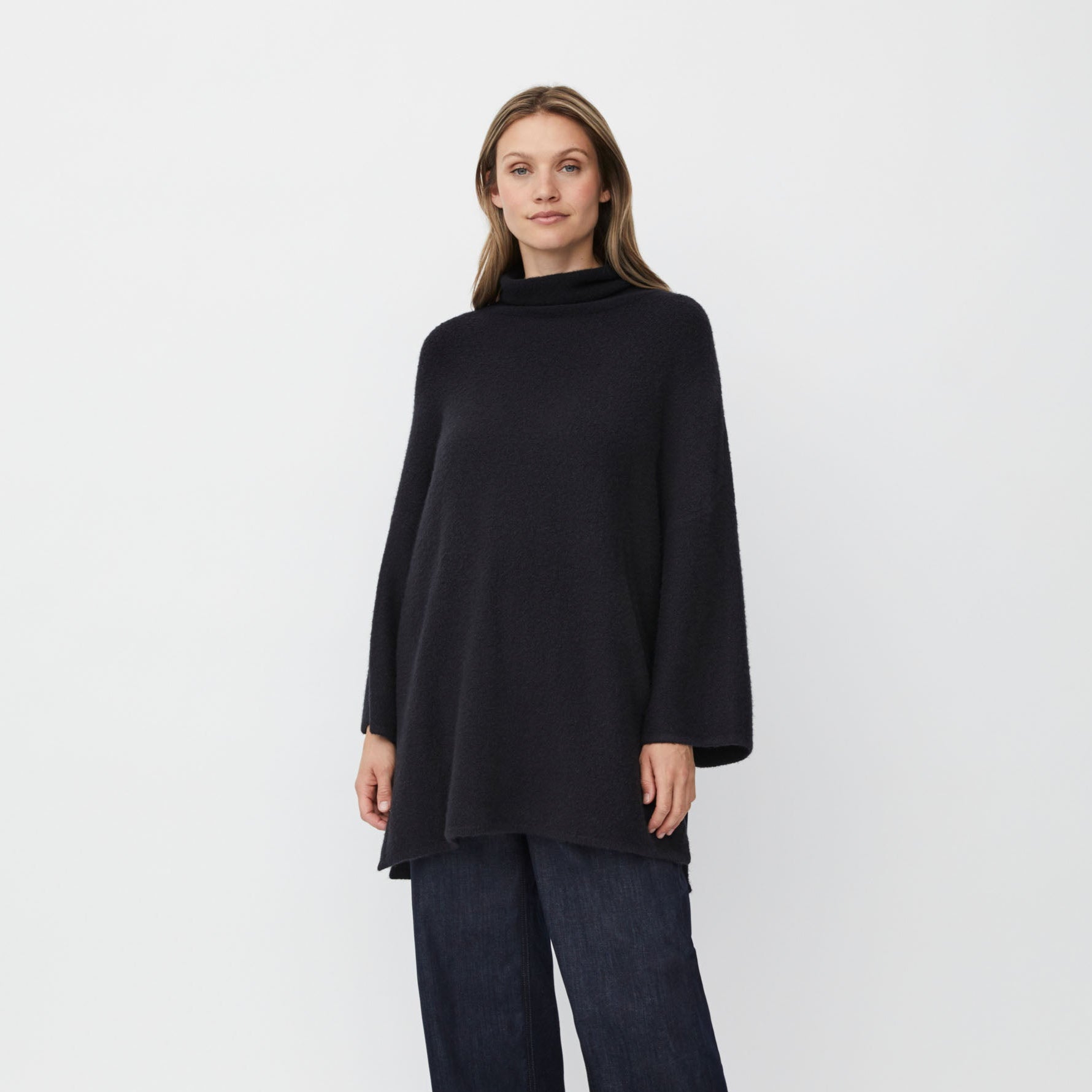 Woman wearing a black tunic and dark jeans on a white background