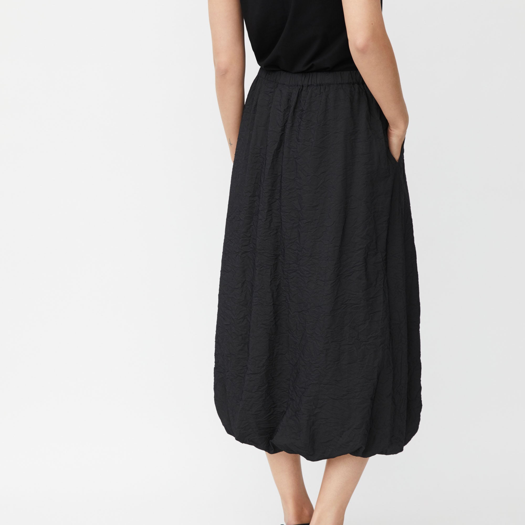 Black midi skirt with a textured, crinkled fabric and a balloon hem.  Elastic waistband.  Side pockets.