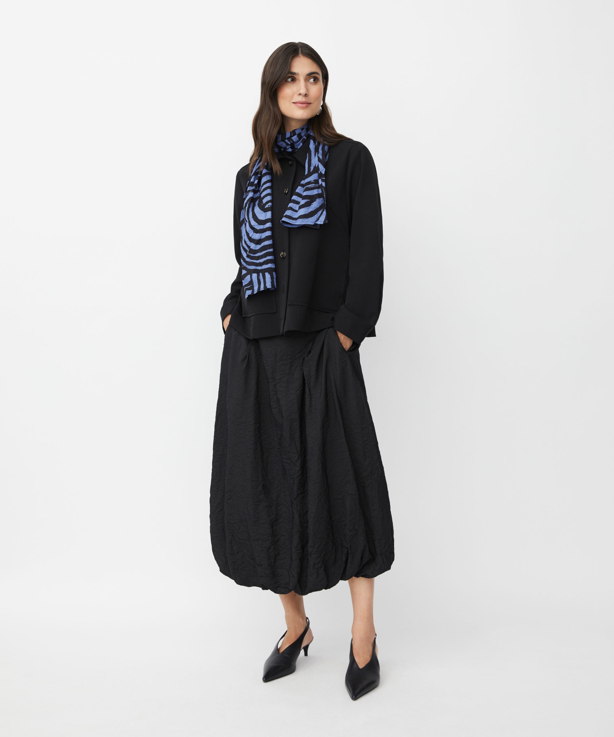 Black cropped button-front jacket, worn with a blue and black patterned scarf and a textured black midi skirt.