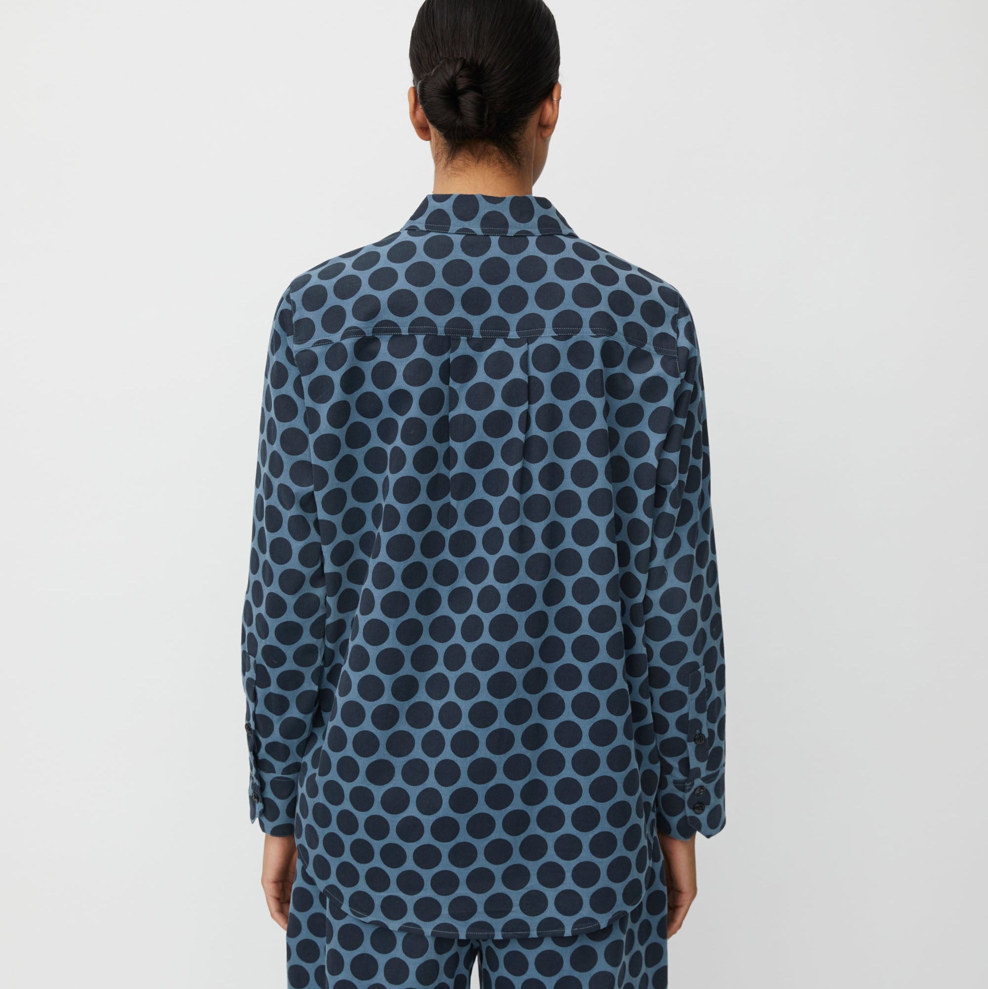 Person wearing a blue polka dot shirt and pants on a white background