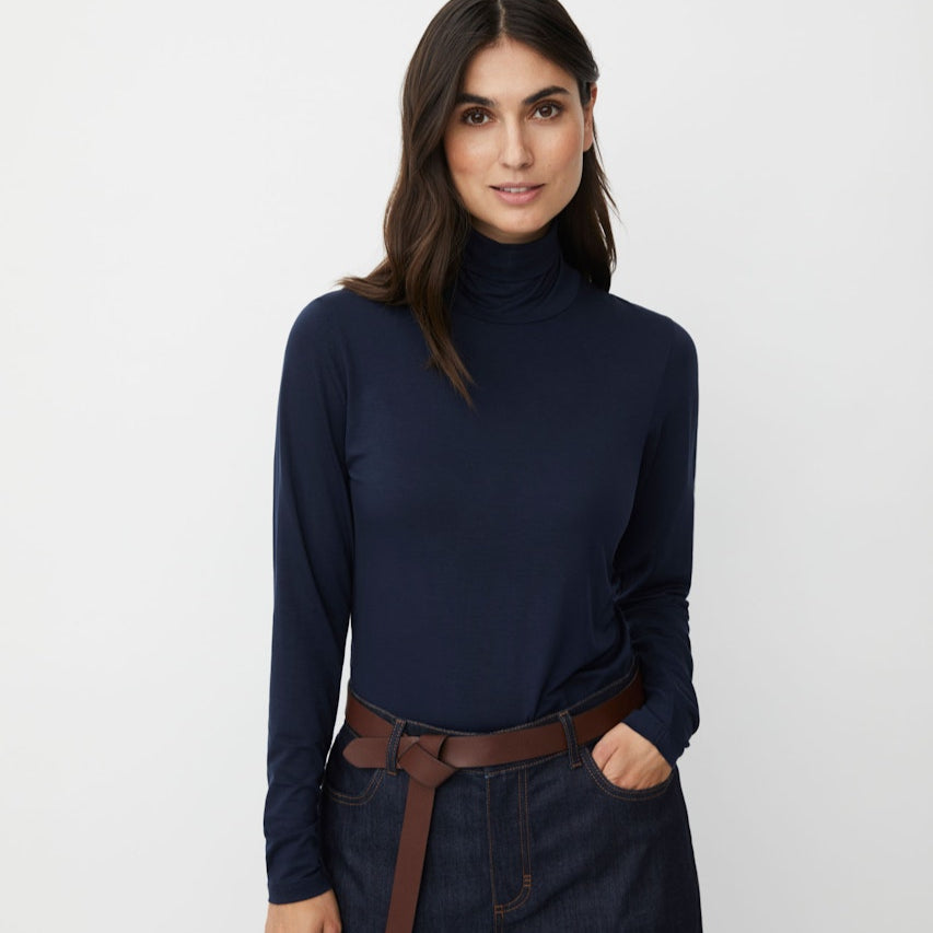 Woman wearing a navy turtleneck and dark jeans against a light gray background