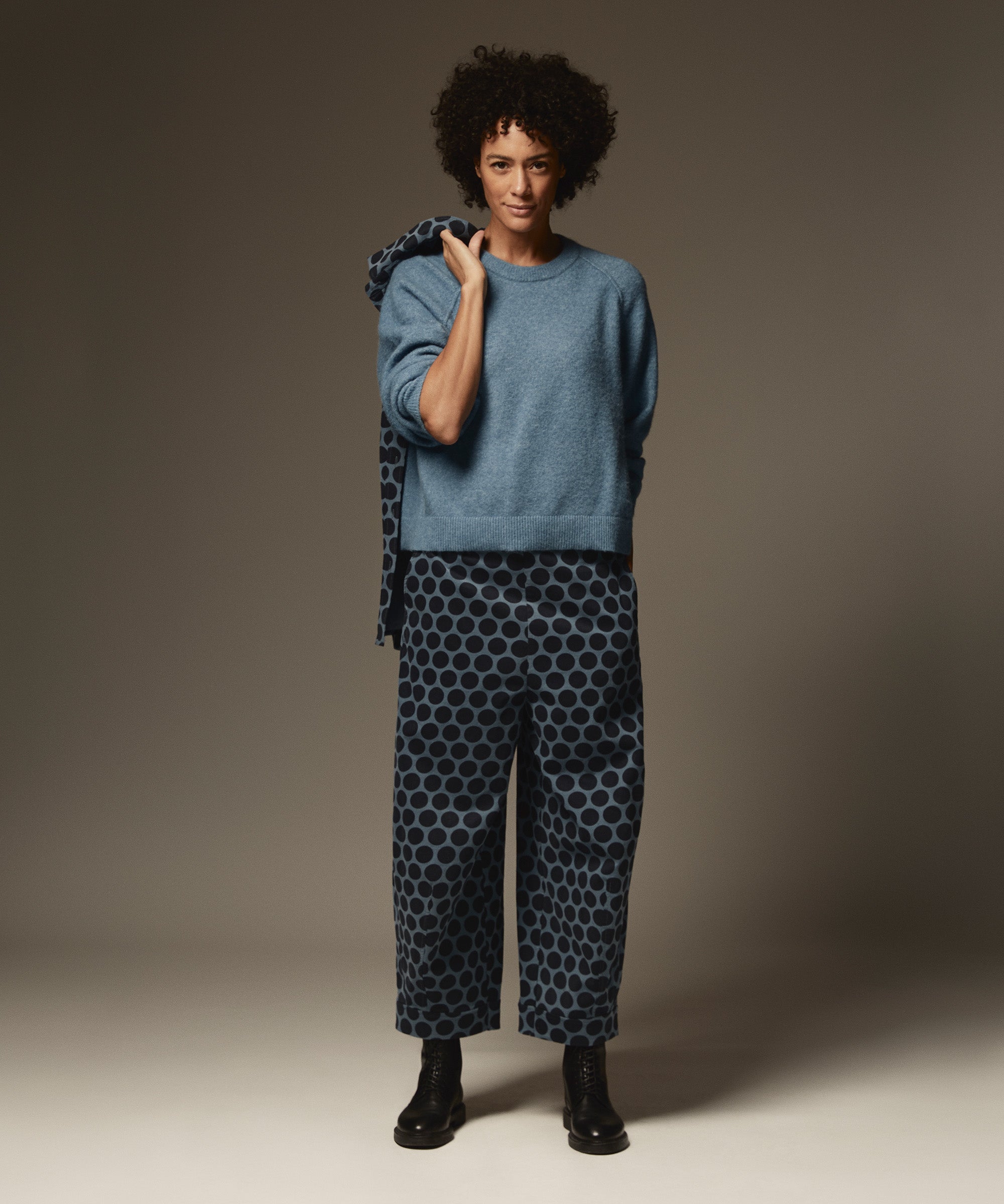Person wearing a blue sweater and patterned pants against a neutral background