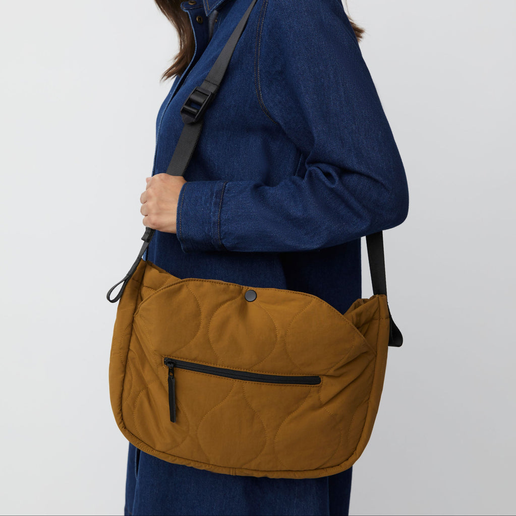 Mustard-colored quilted shoulder bag with a black adjustable strap and zippered pocket.
