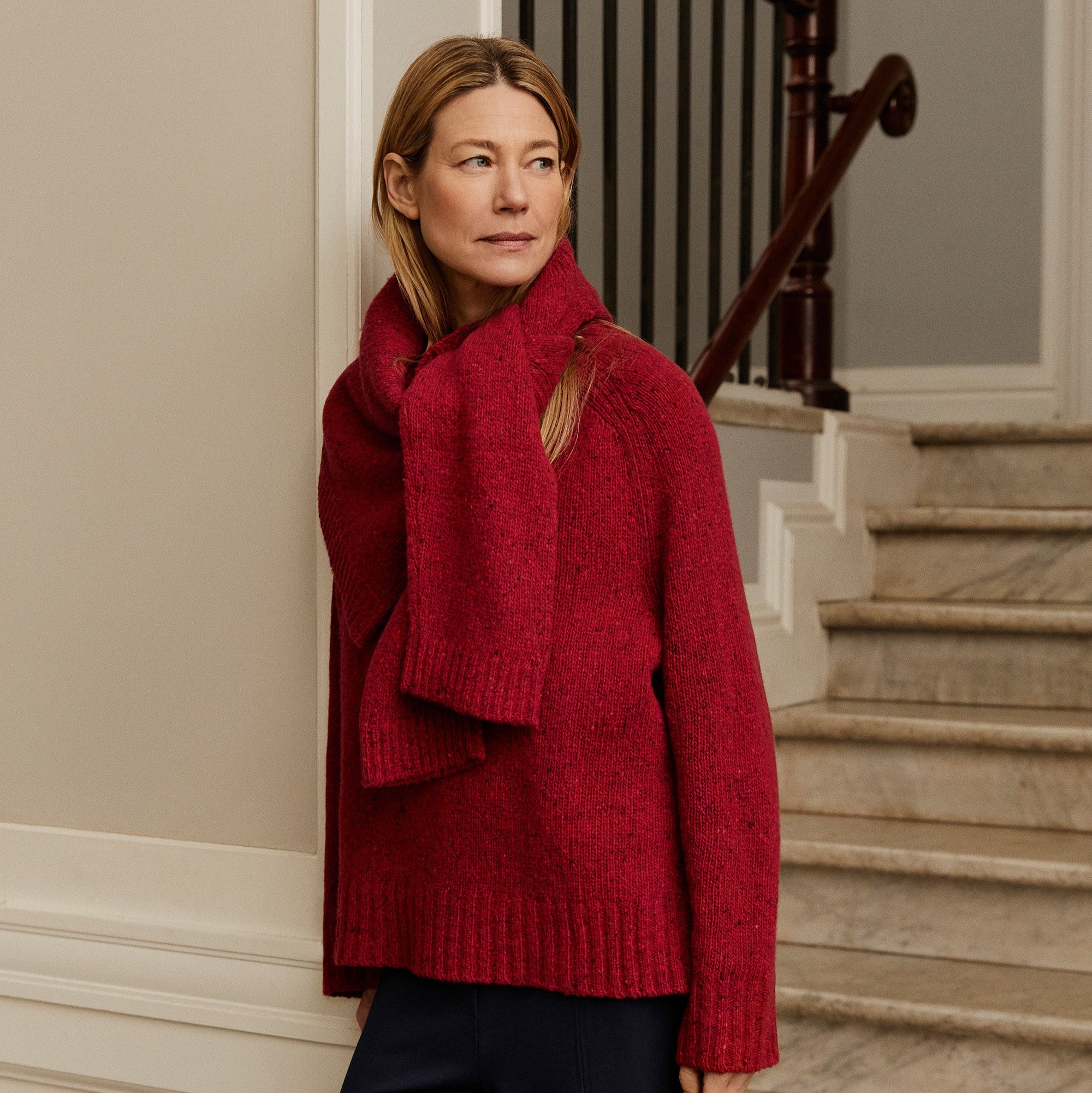 Woman wearing a red sweater and scarf standing on a staircase.