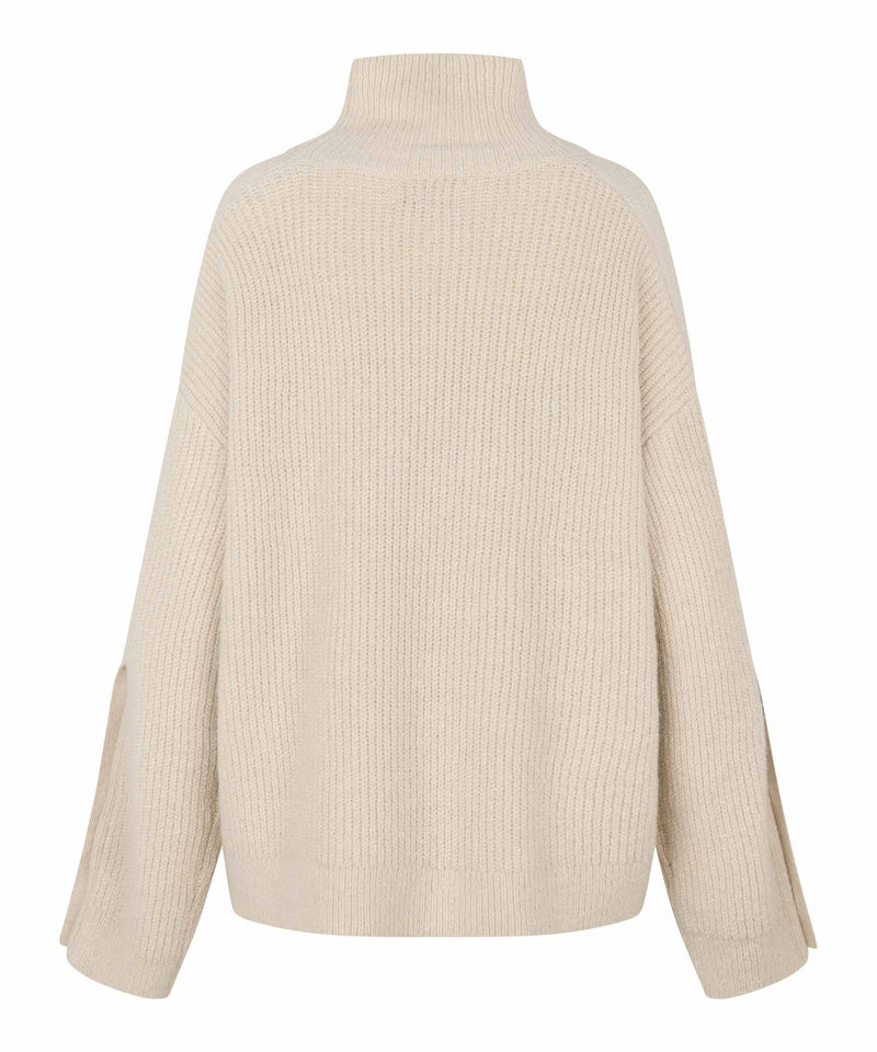 A cream-colored ribbed knit turtleneck sweater shown from the back, featuring long sleeves with side slits, set against a plain white background.