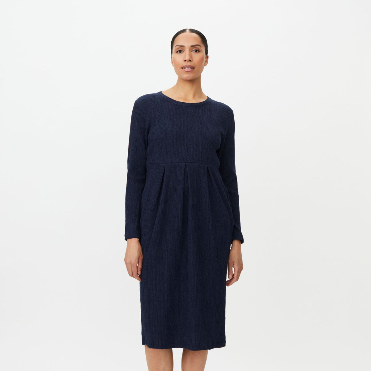 A woman modeling a long-sleeve navy blue midi dress with a gathered waist, standing against a plain white studio background.