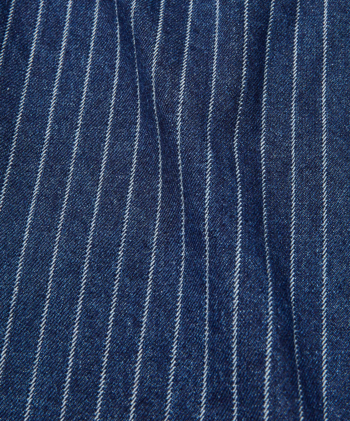 A close-up of dark blue denim fabric with thin white vertical pinstripes.