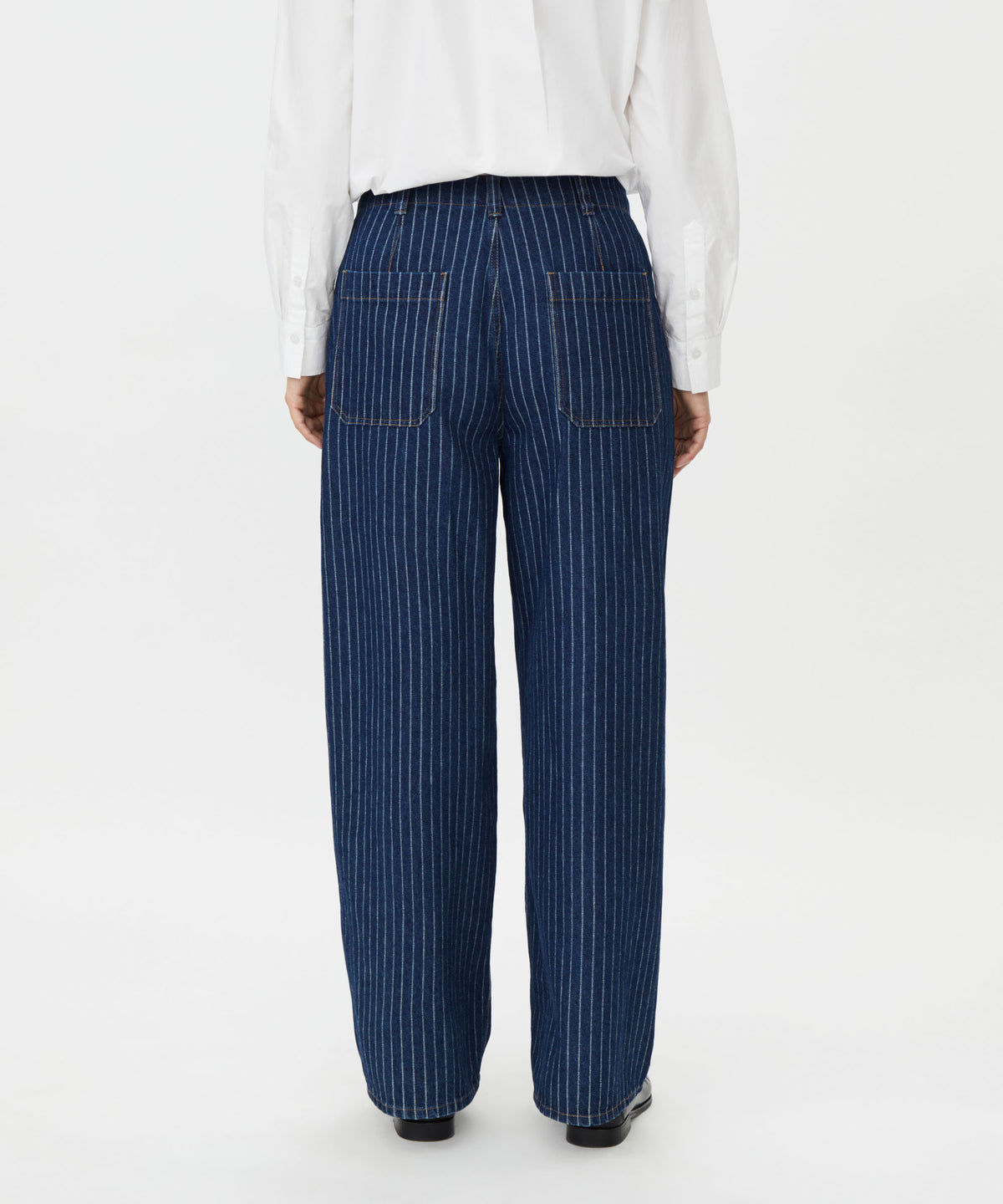 A person shown from the back wearing dark blue pinstriped trousers with a white shirt and black shoes, photographed against a plain light gray studio background.