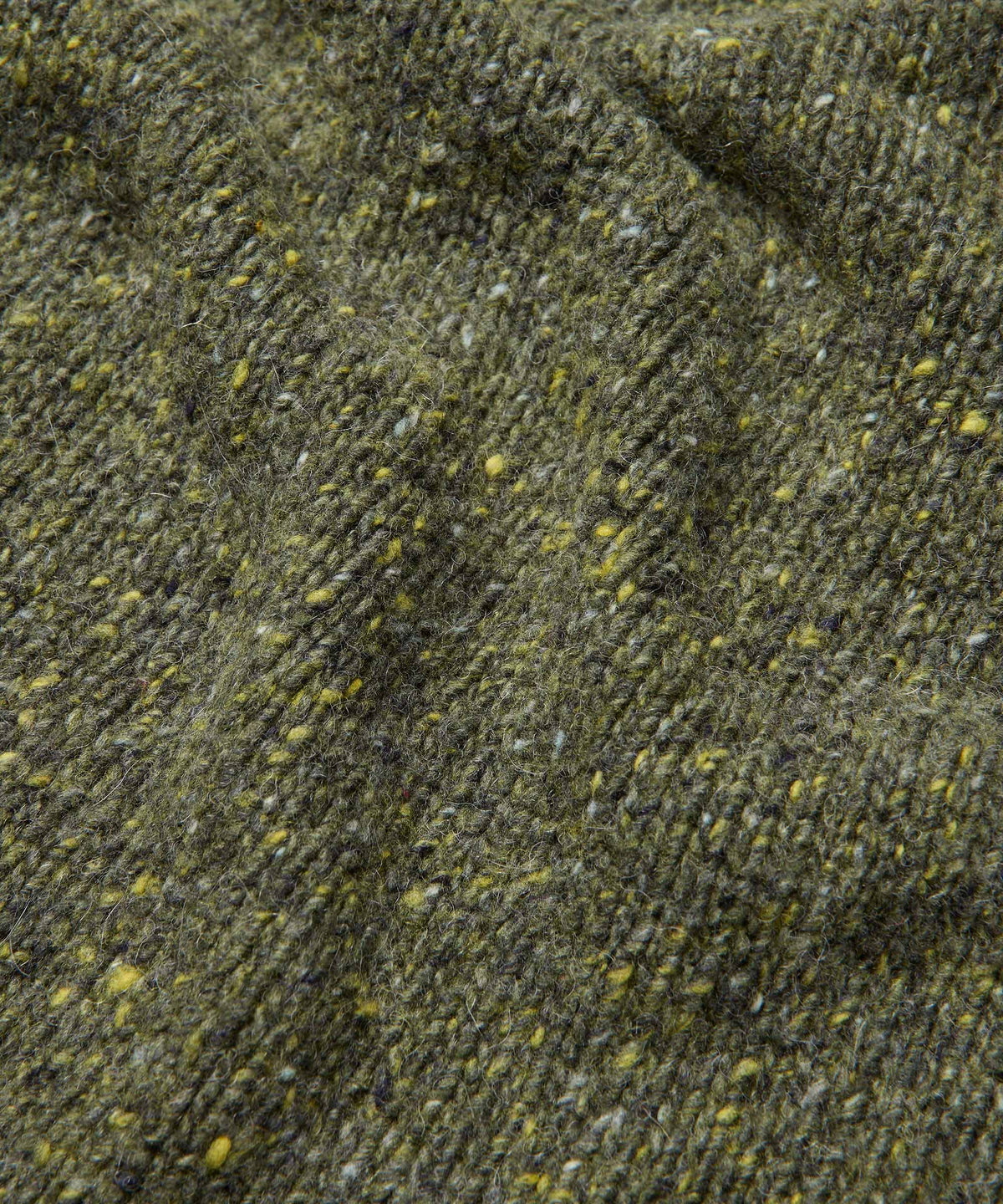 Close-up of a textured tweed fabric in olive green with flecks of yellow, gray, and white.