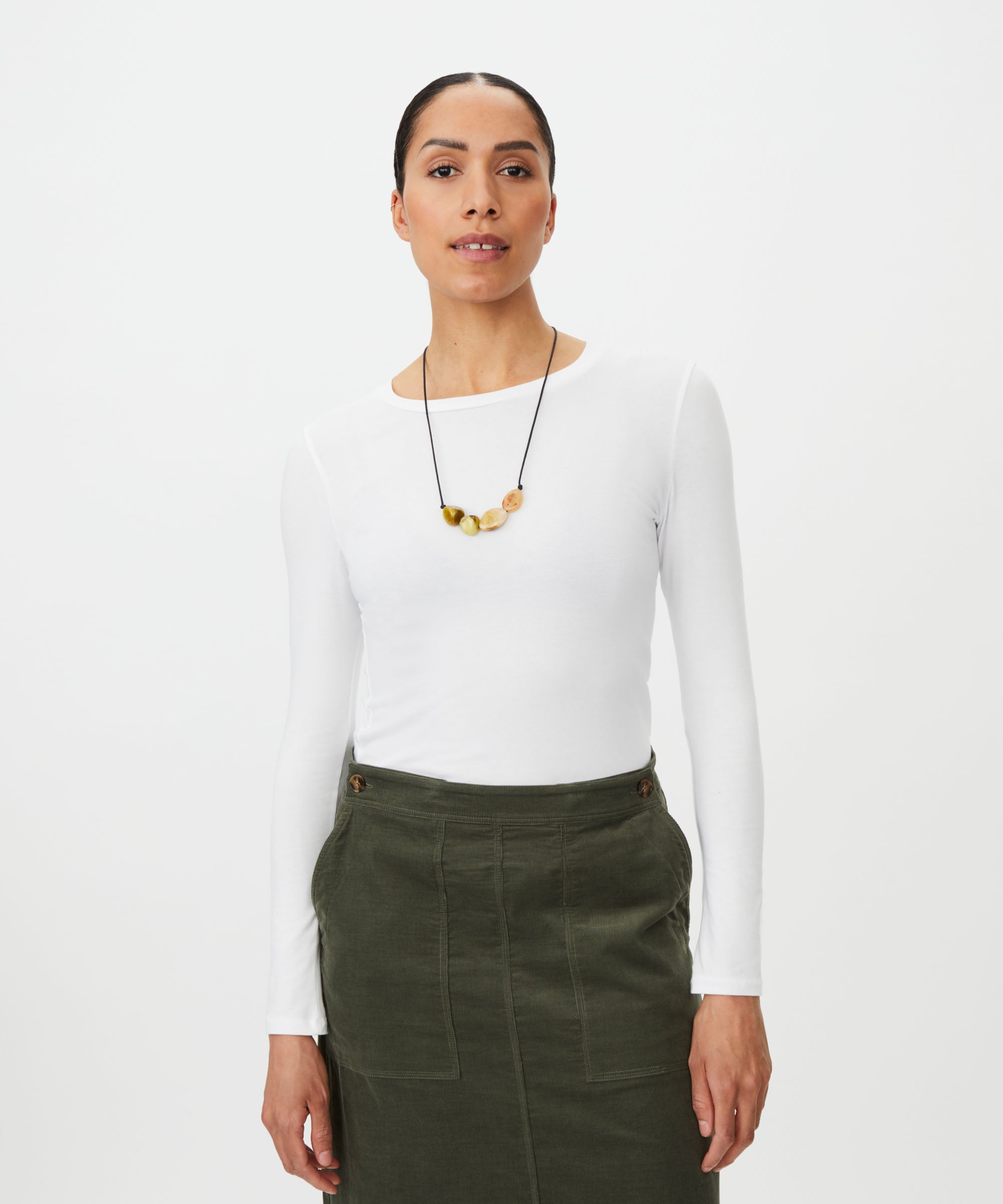 Woman wearing a white long-sleeve top and green pants on a white background