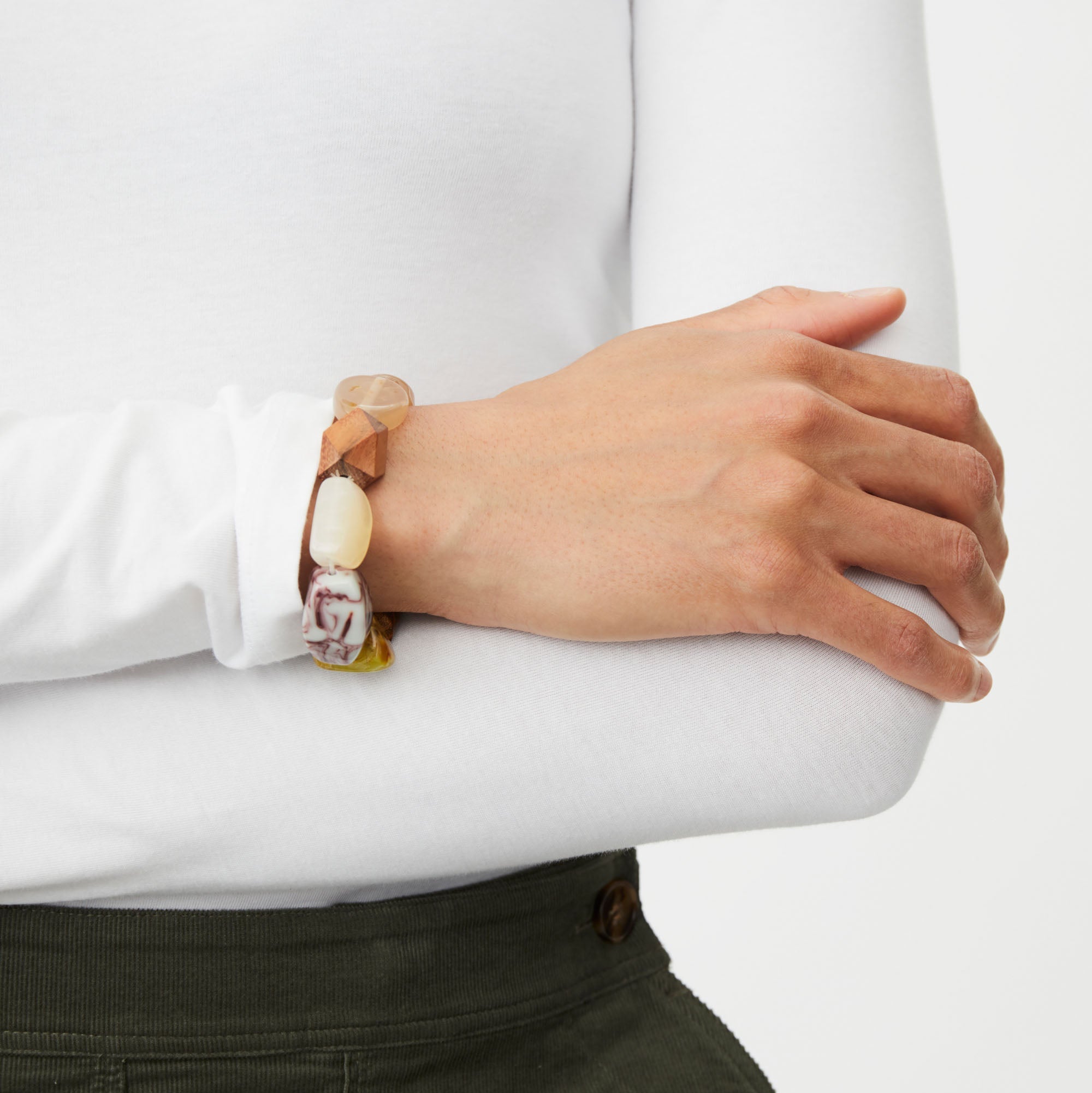 Person wearing a white shirt and green pants with a bracelet on a plain background