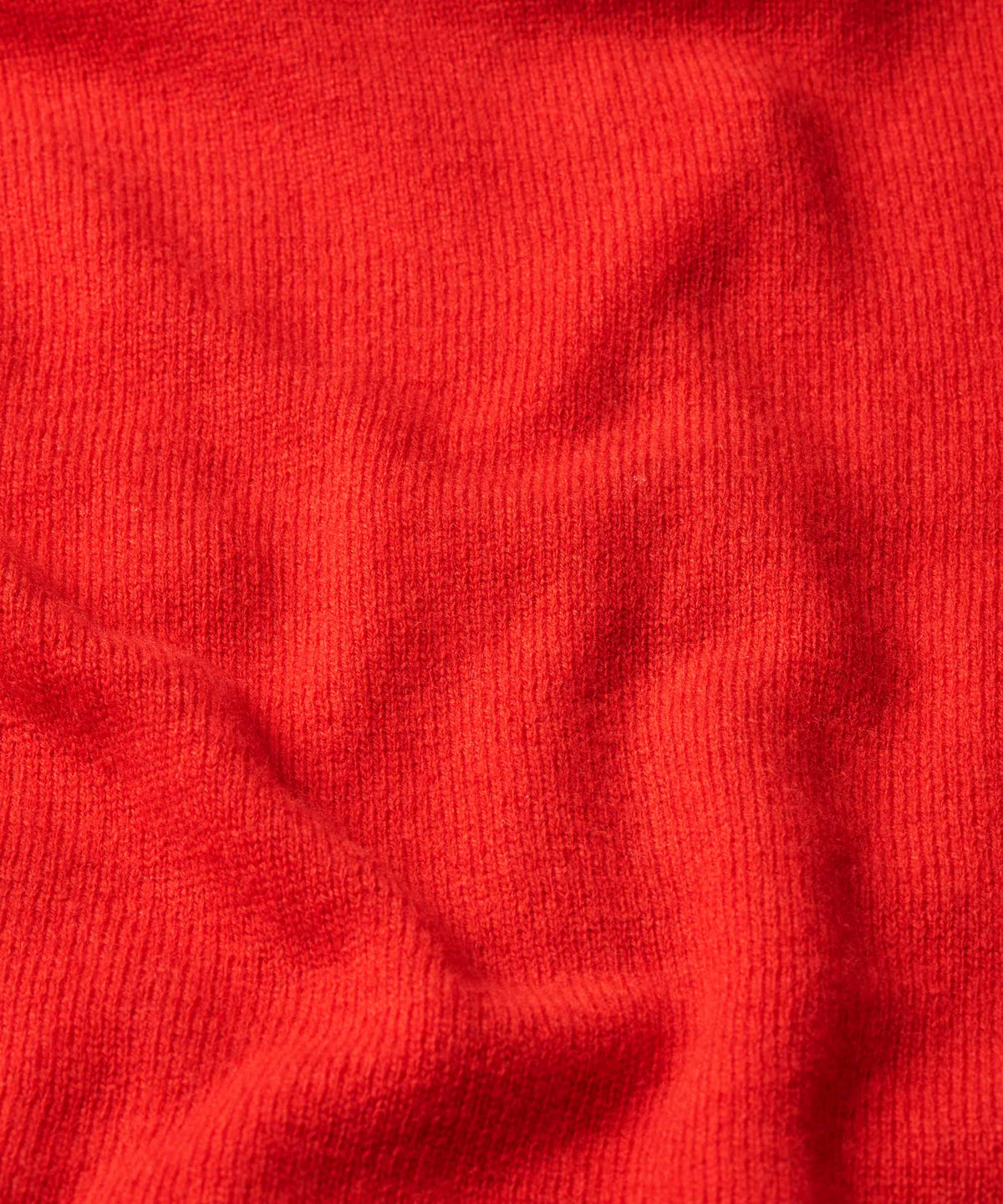 A close-up of bright red ribbed knit fabric with soft folds and shadows.