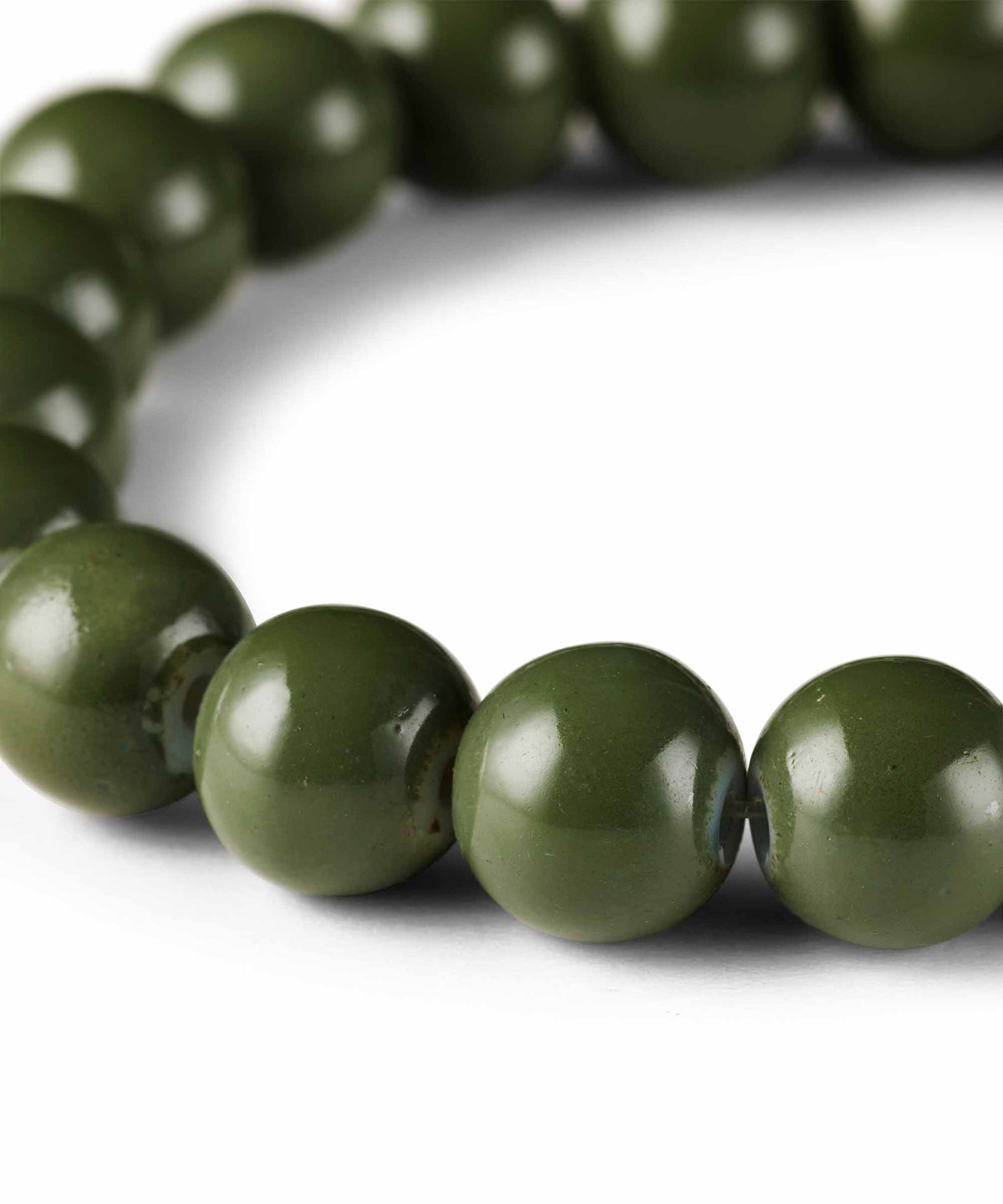 A close-up of glossy olive green round beads, likely part of a beaded bracelet or necklace, arranged in a curve on a white background.