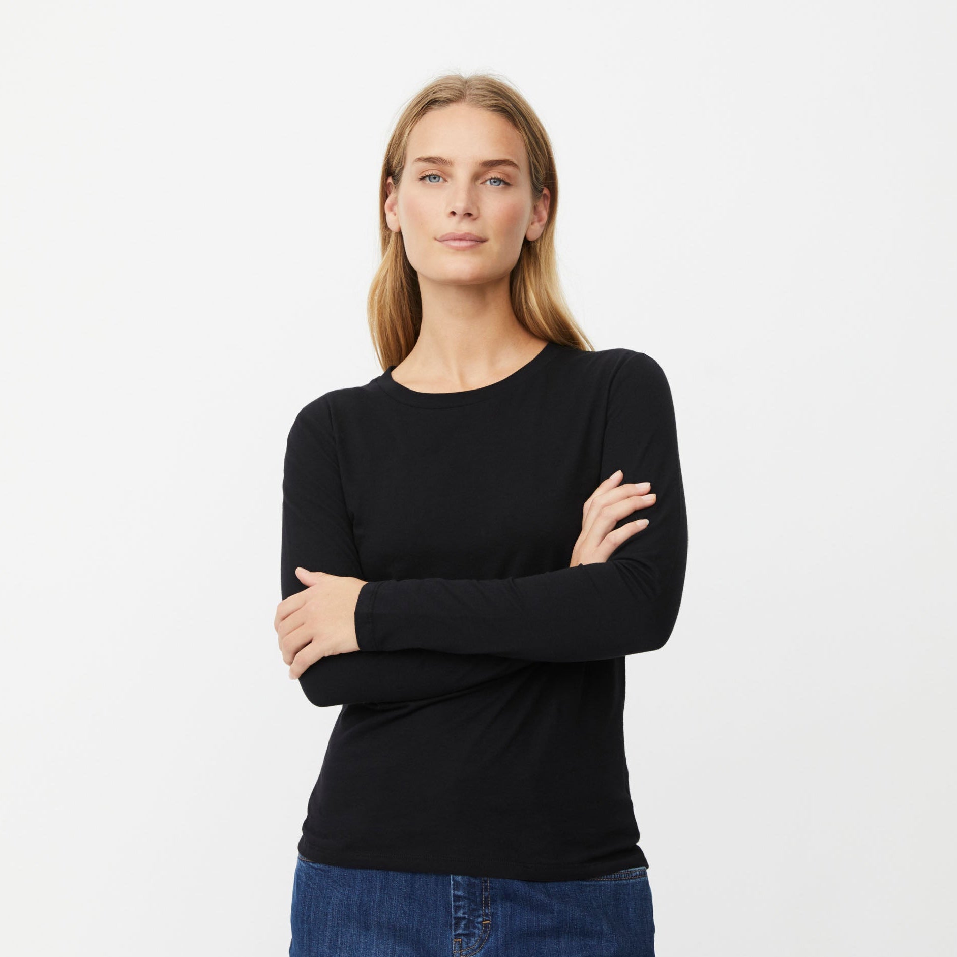 A woman modeling a black long-sleeve crewneck top with blue jeans, standing against a plain white studio background.