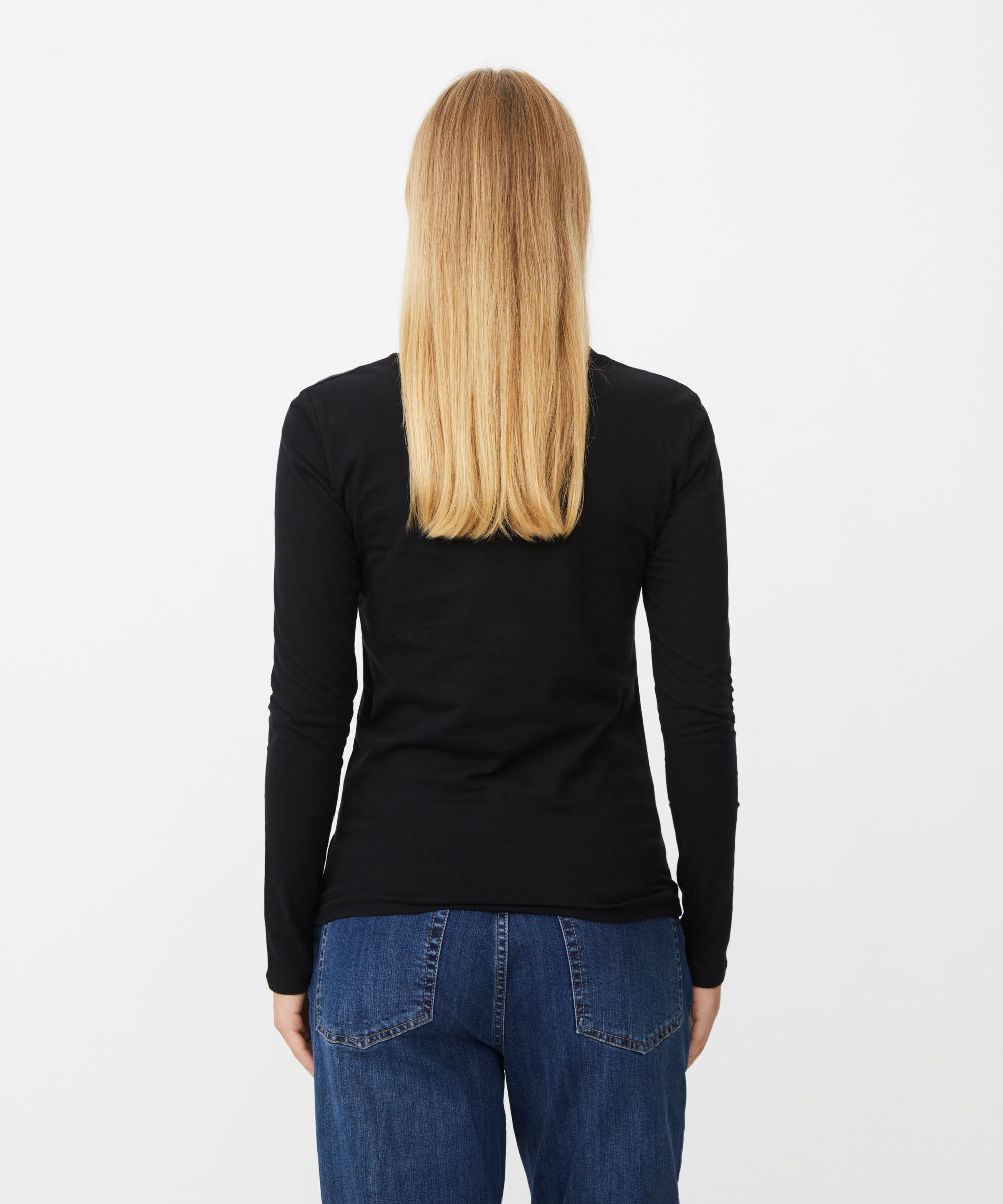 A woman viewed from the back wearing a fitted black long-sleeve top and blue jeans against a plain light gray studio background.