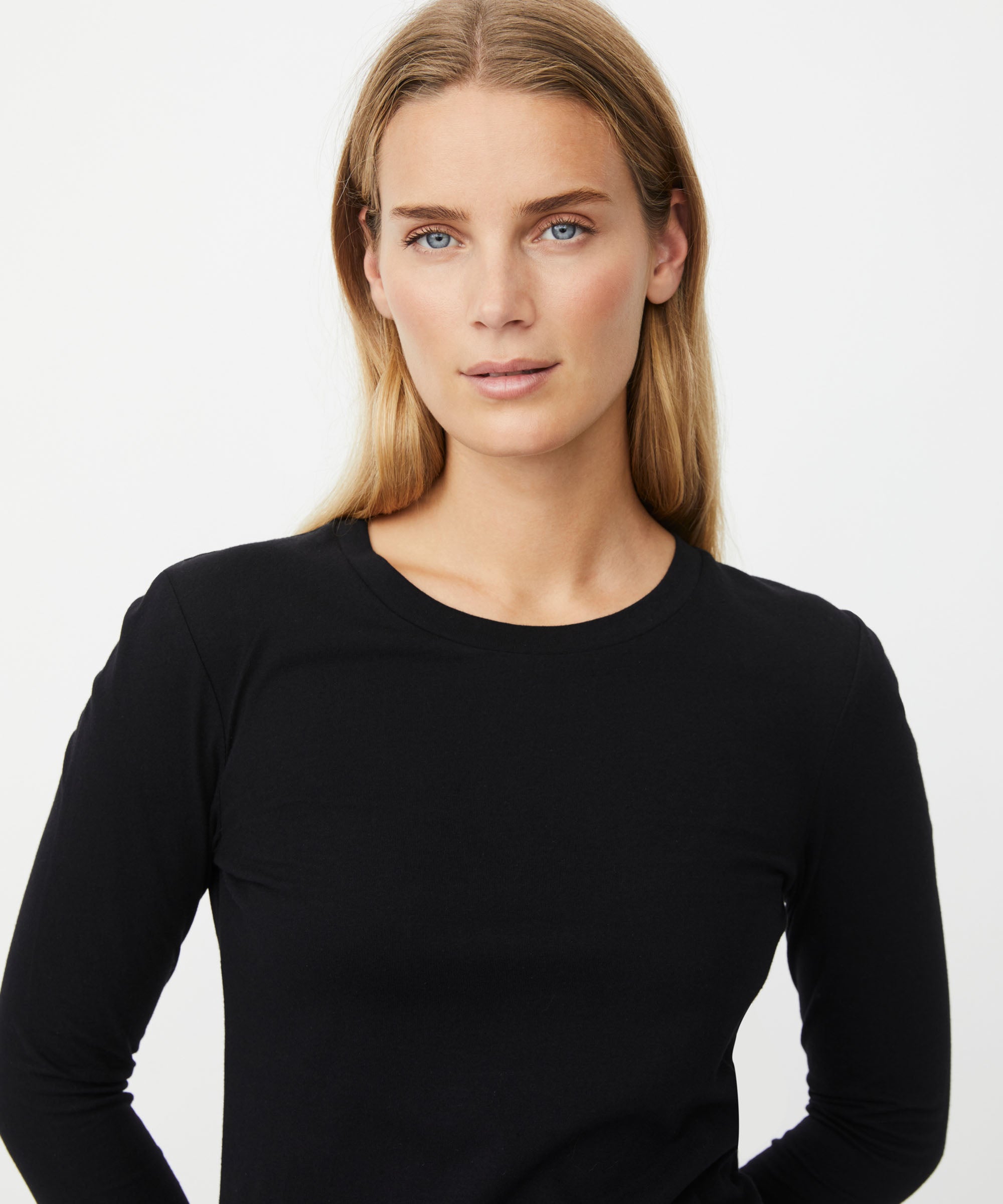 A woman with blonde hair wearing a black long-sleeve crewneck top, photographed against a plain light gray studio background.