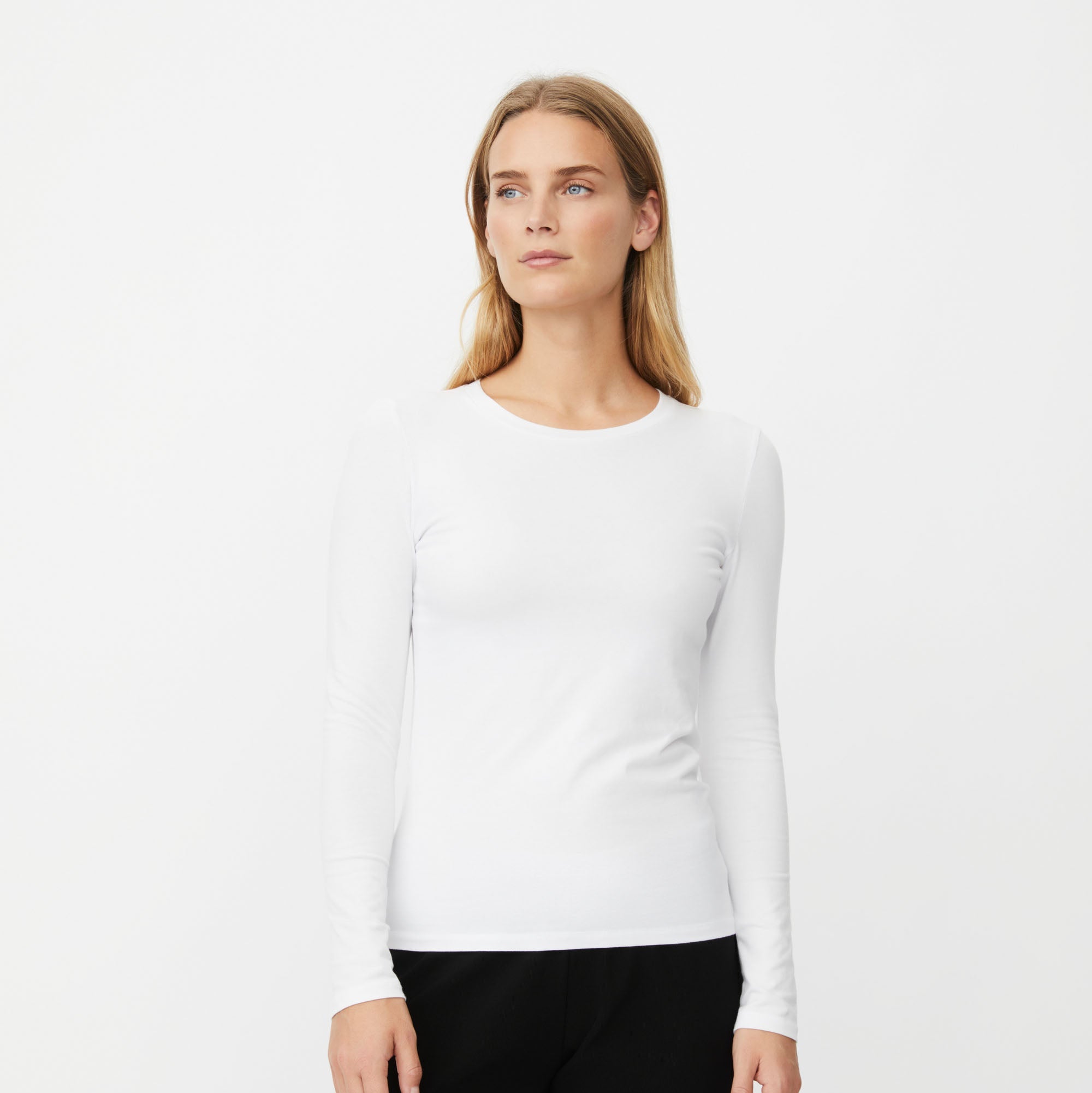 A woman modeling a white long-sleeve crewneck top against a plain white studio background.