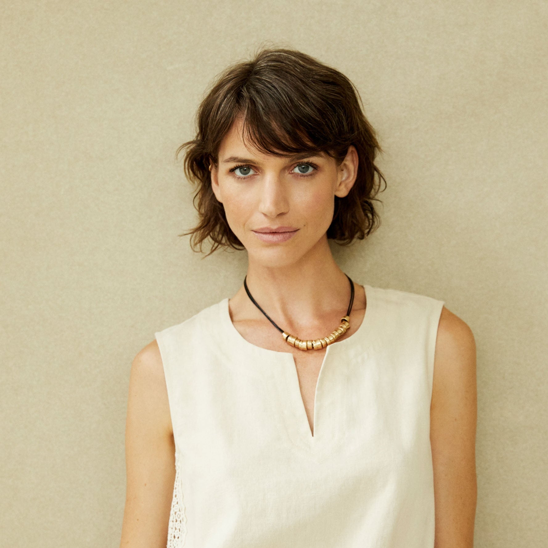 Woman wearing a white sleeveless top against a beige background