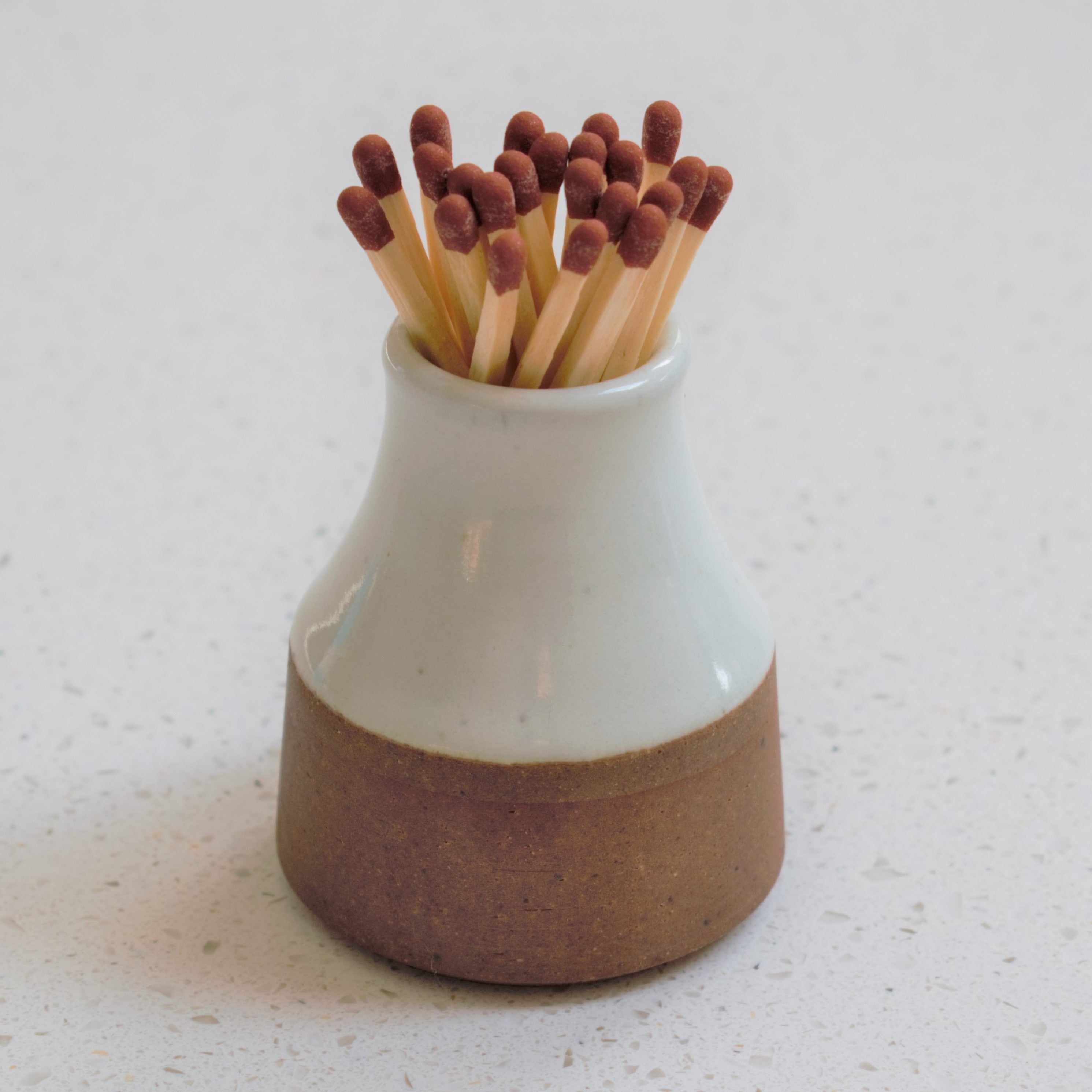 A ceramic match holder with a brown and white glaze, filled with wooden matches with dark brown tips.