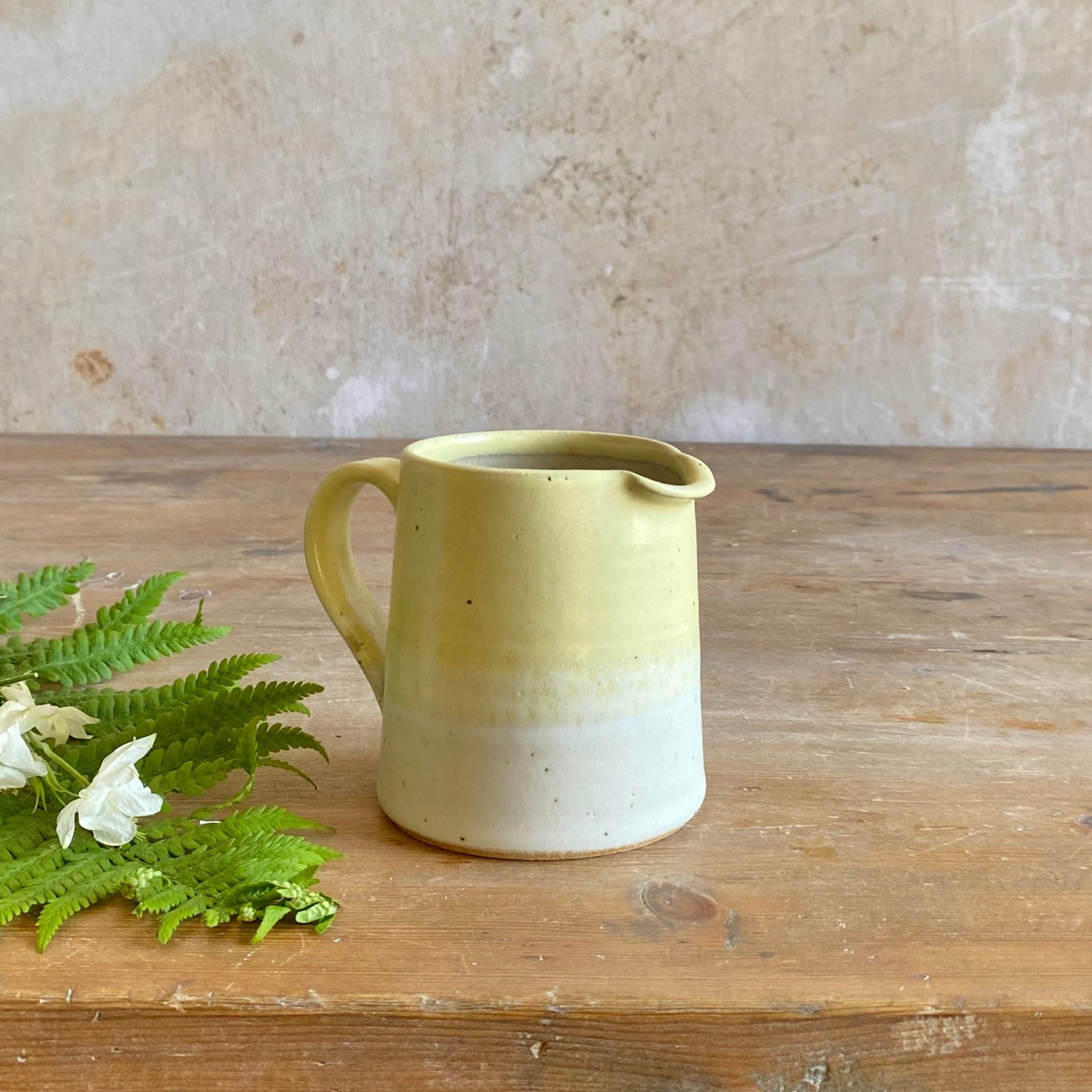Small, pale yellow ceramic creamer or milk jug with a white base, featuring a slightly uneven, hand-thrown appearance.