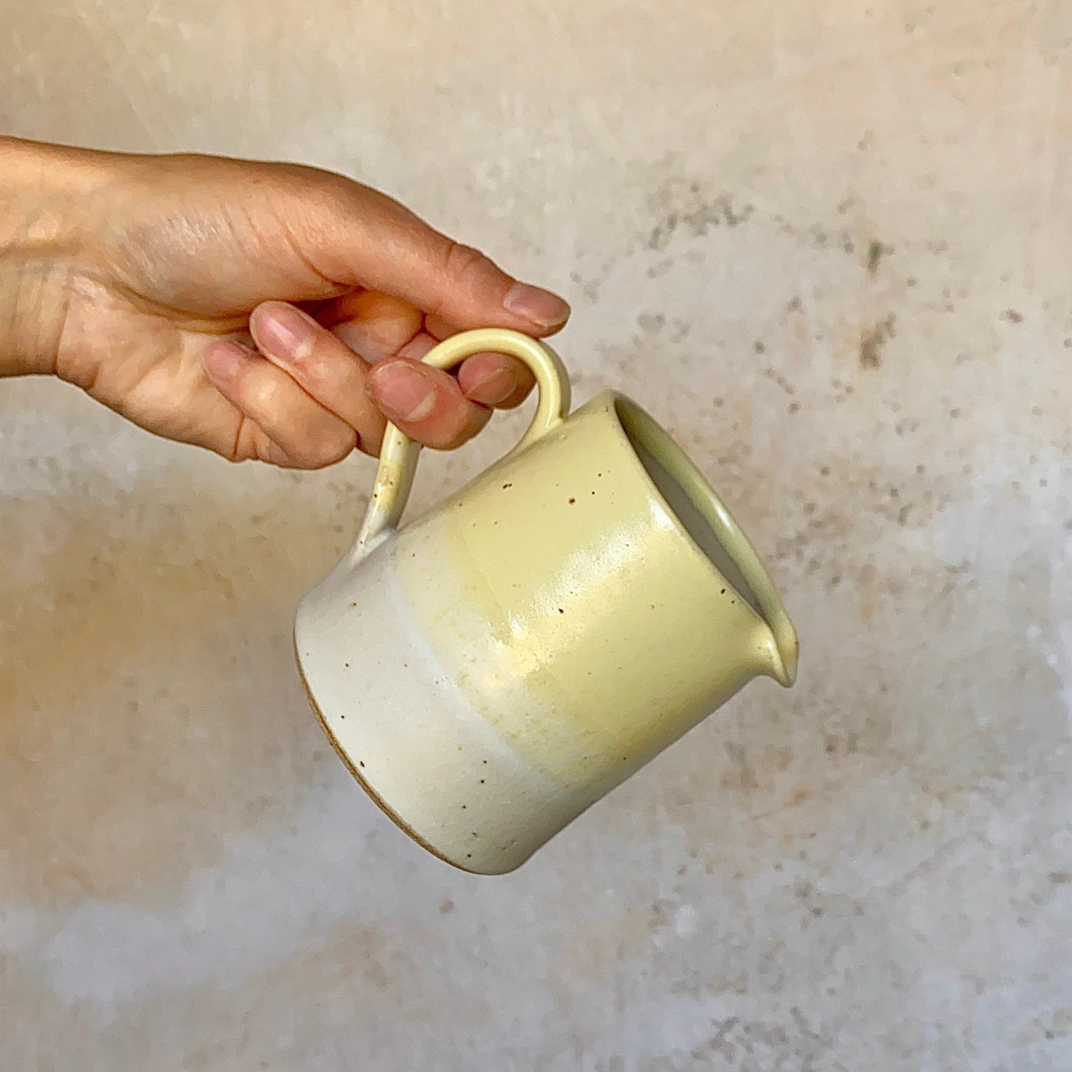 Small, pale yellow ceramic creamer with a speckled, ombre design, transitioning to off-white at the base.
