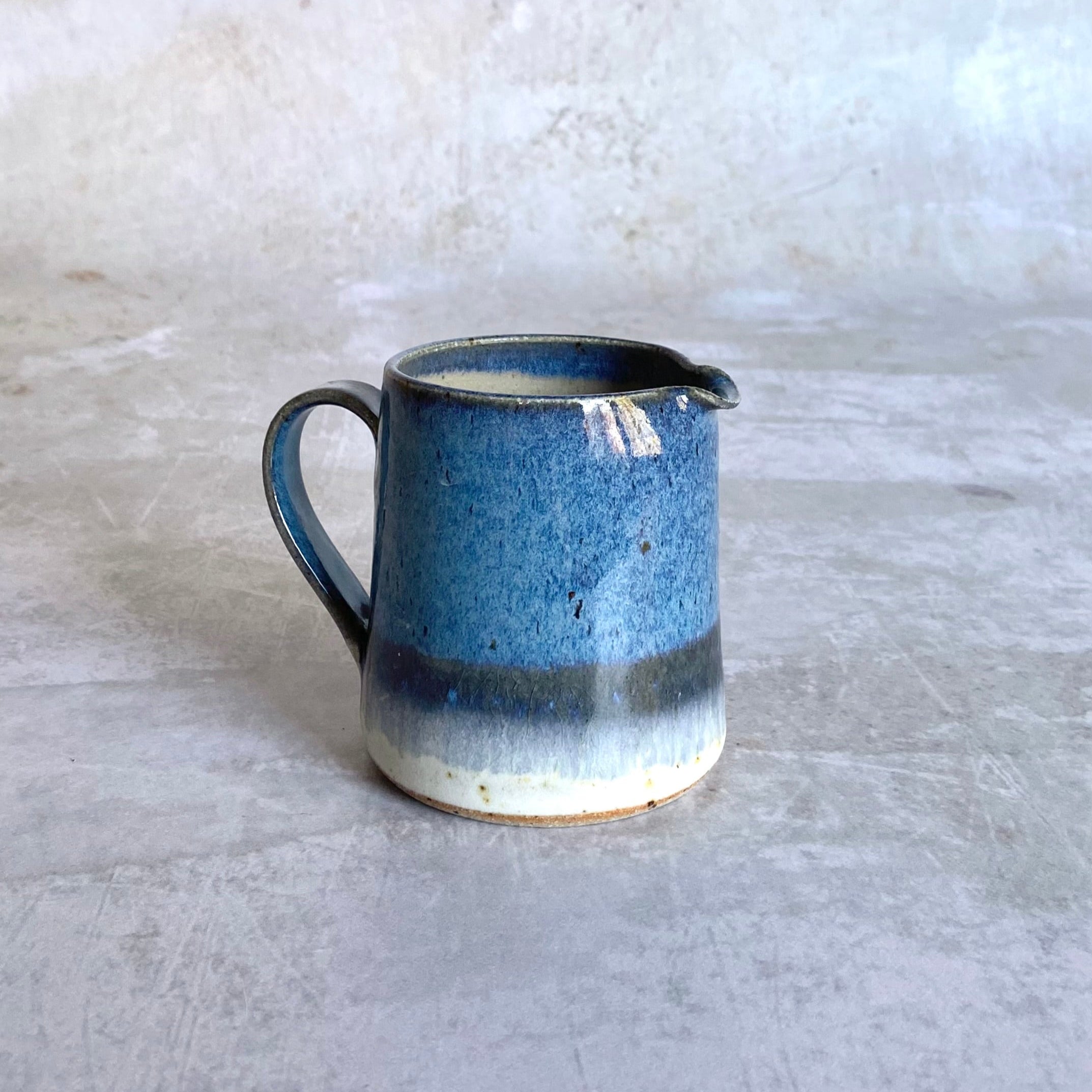 Small ceramic creamer in shades of blue, with a handle and a subtle off-white band at the base.