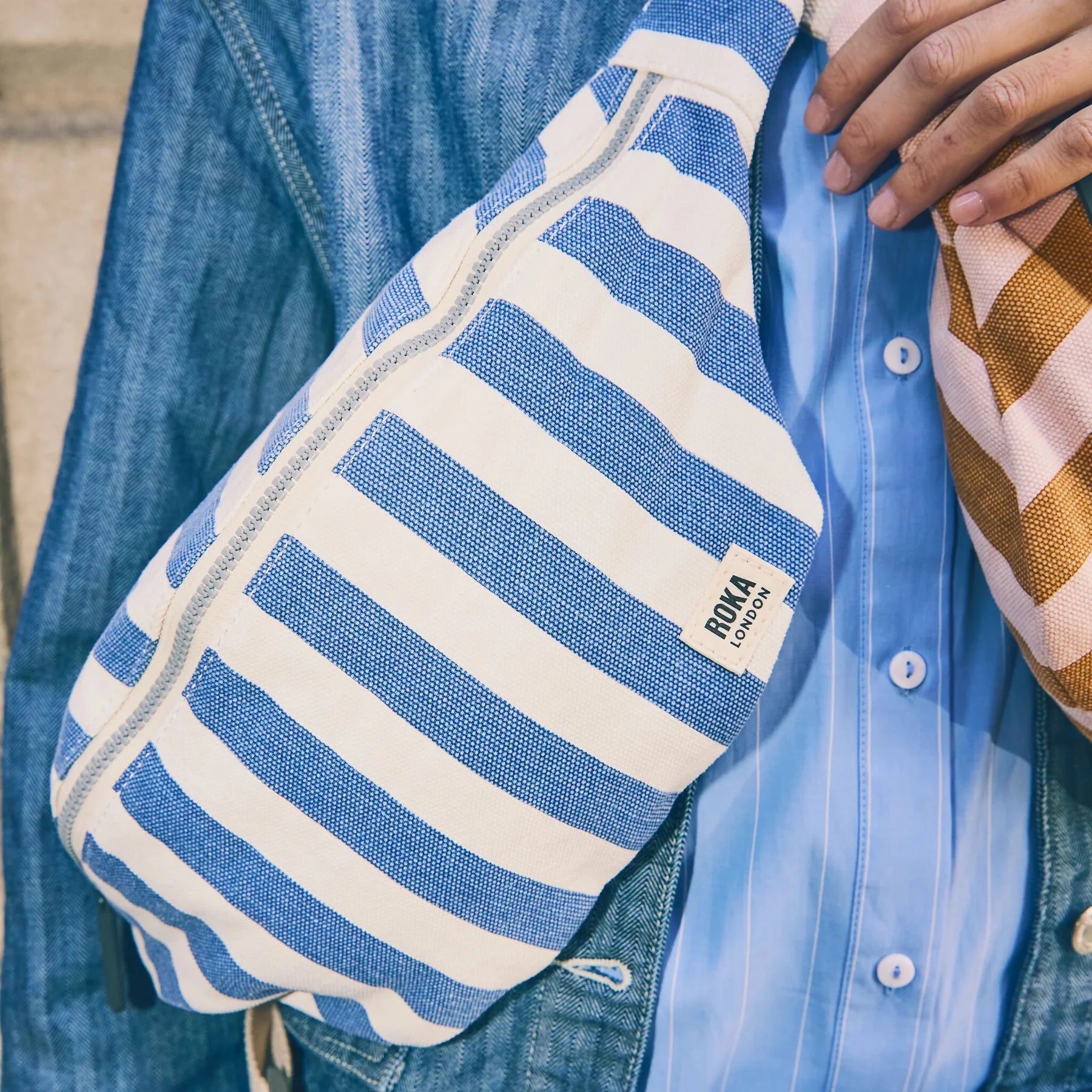Blue and white striped bag with 'Kona' branding held by a person wearing a blue shirt and jeans.