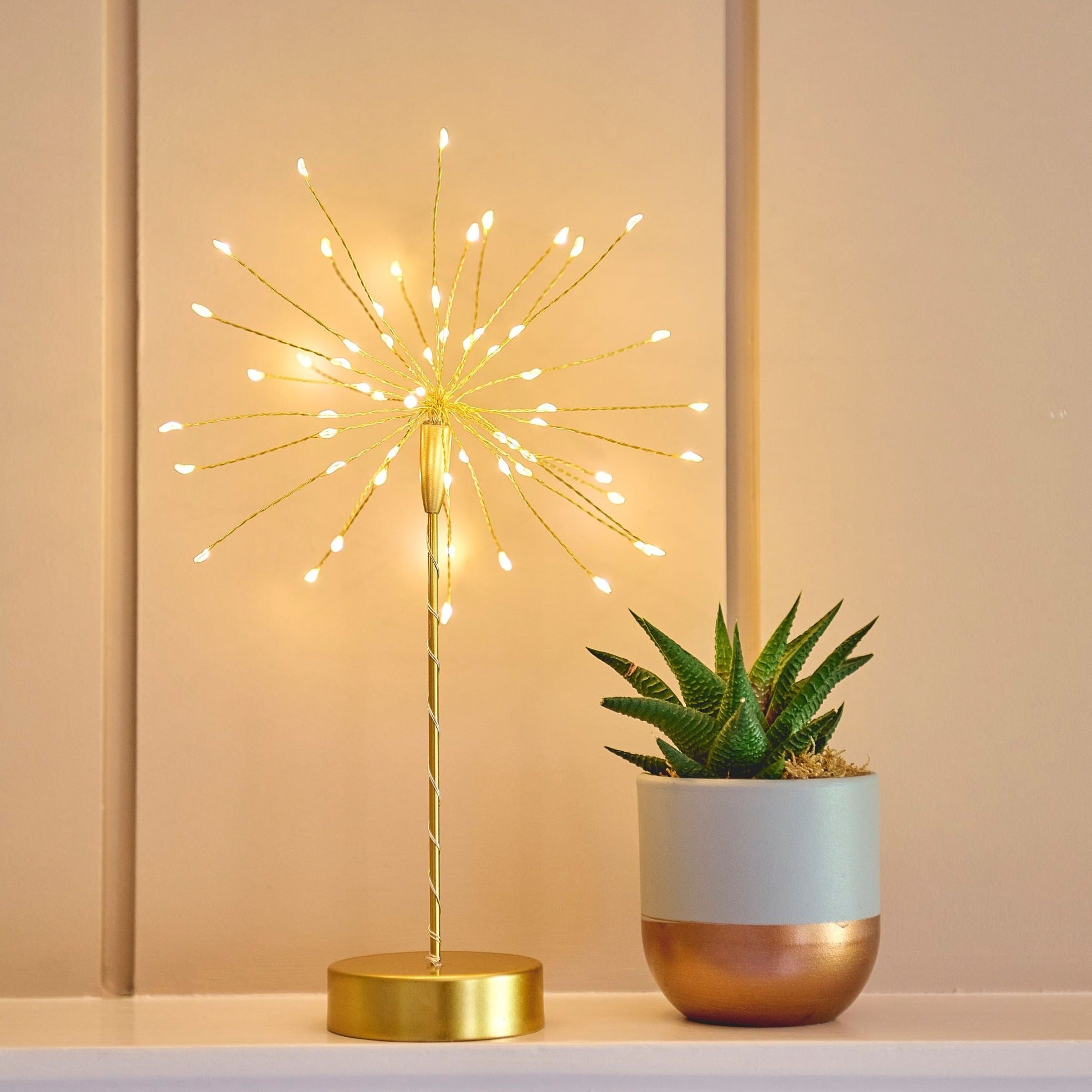 Gold metal table lamp with numerous small warm-white LED lights extending outwards, creating a firework-like effect.