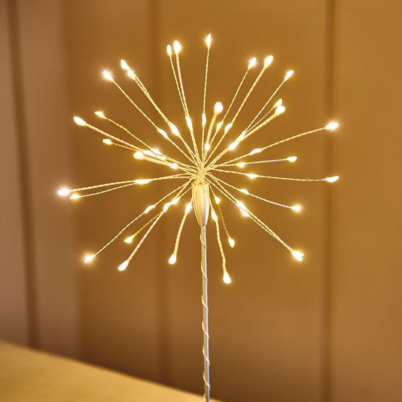 LED firework light display on a thin metal stem.  Numerous small warm-white lights radiate outwards.