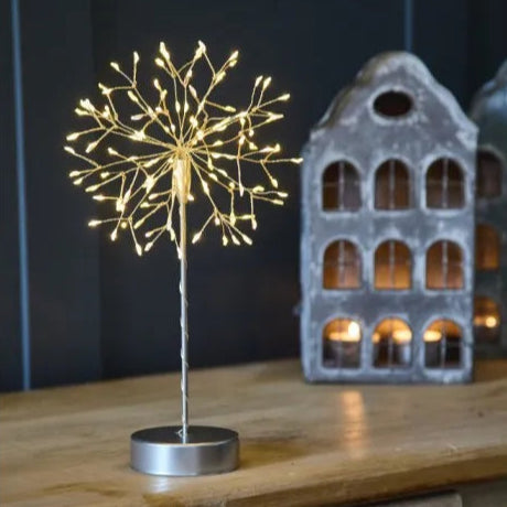Decorative light fixture resembling a dandelion on a wooden surface with a dark background.