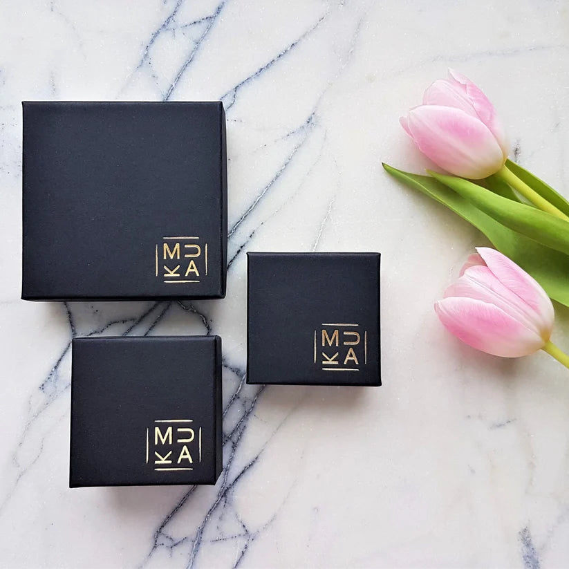 Three black square boxes of varying sizes, each with a gold logo, appear on a marble surface.