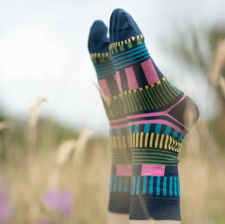 Colorful patterned socks by Donna Wilson, featuring blue, pink, green, and yellow stripes, set against a natural background.